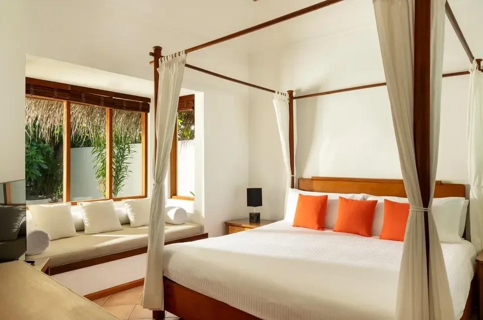 Deluxe Beach Villa bedroom with a four-poster bed dressed in orange cushions, garden views through the window seat
