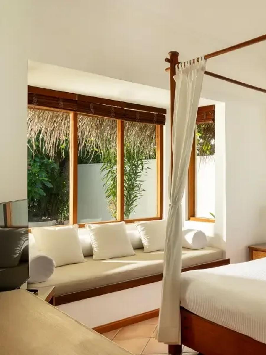 Deluxe Beach Villa bedroom with a four-poster bed dressed in orange cushions, garden views through the window seat