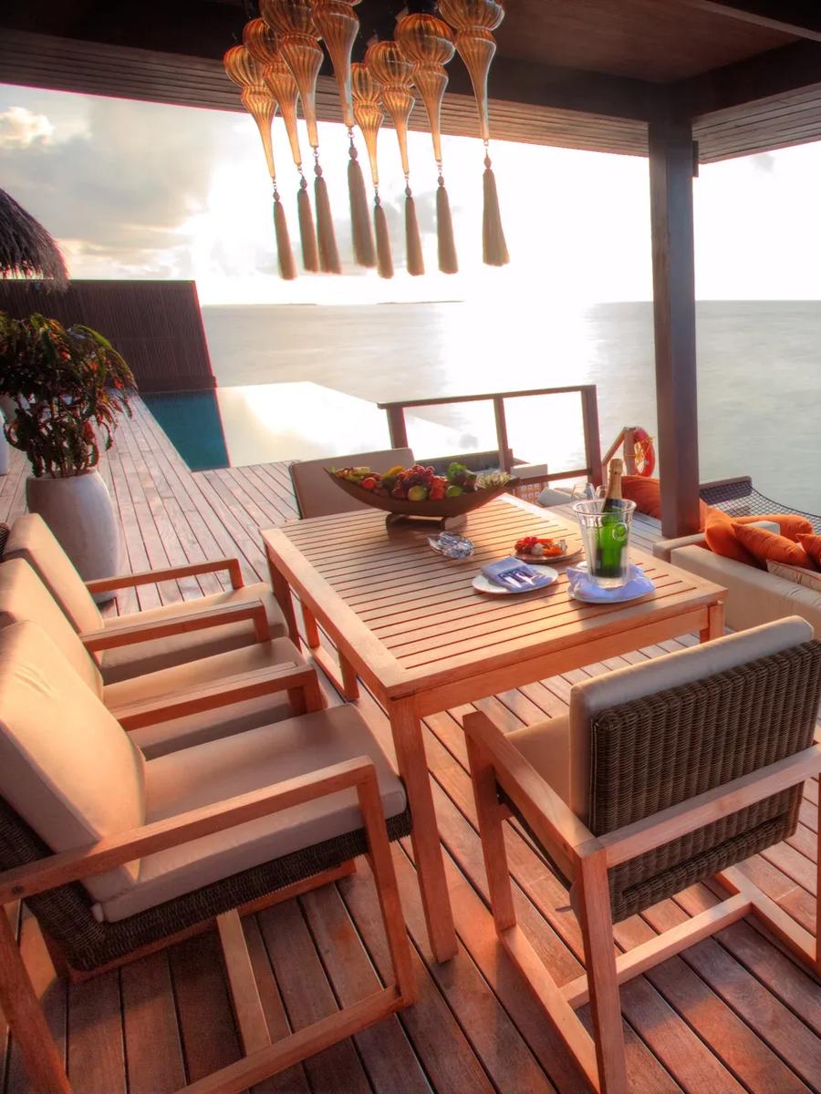 The Royal Ocean Suite's overwater dining deck at sunset, a hanging lantern chandelier above the table and open ocean beyond the netting