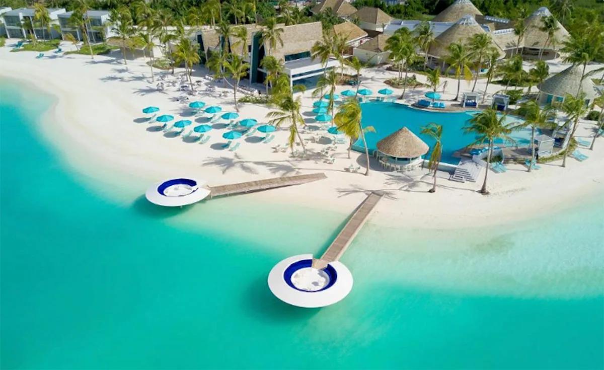 Kandima's main pool and two circular overwater sundeck platforms, seen from above, with the beach and palm-lined guest rooms behind
