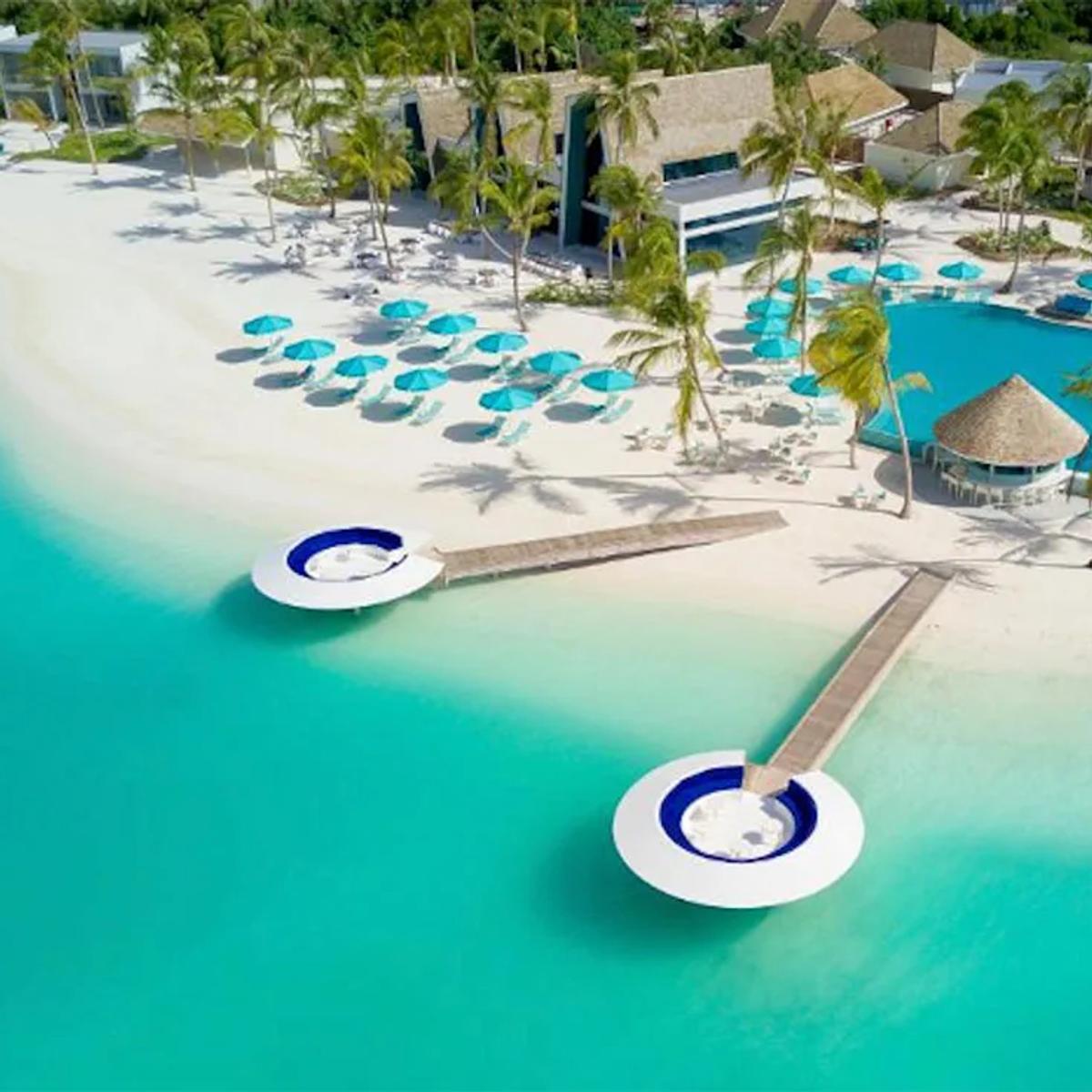 Kandima's main pool and two circular overwater sundeck platforms, seen from above, with the beach and palm-lined guest rooms behind