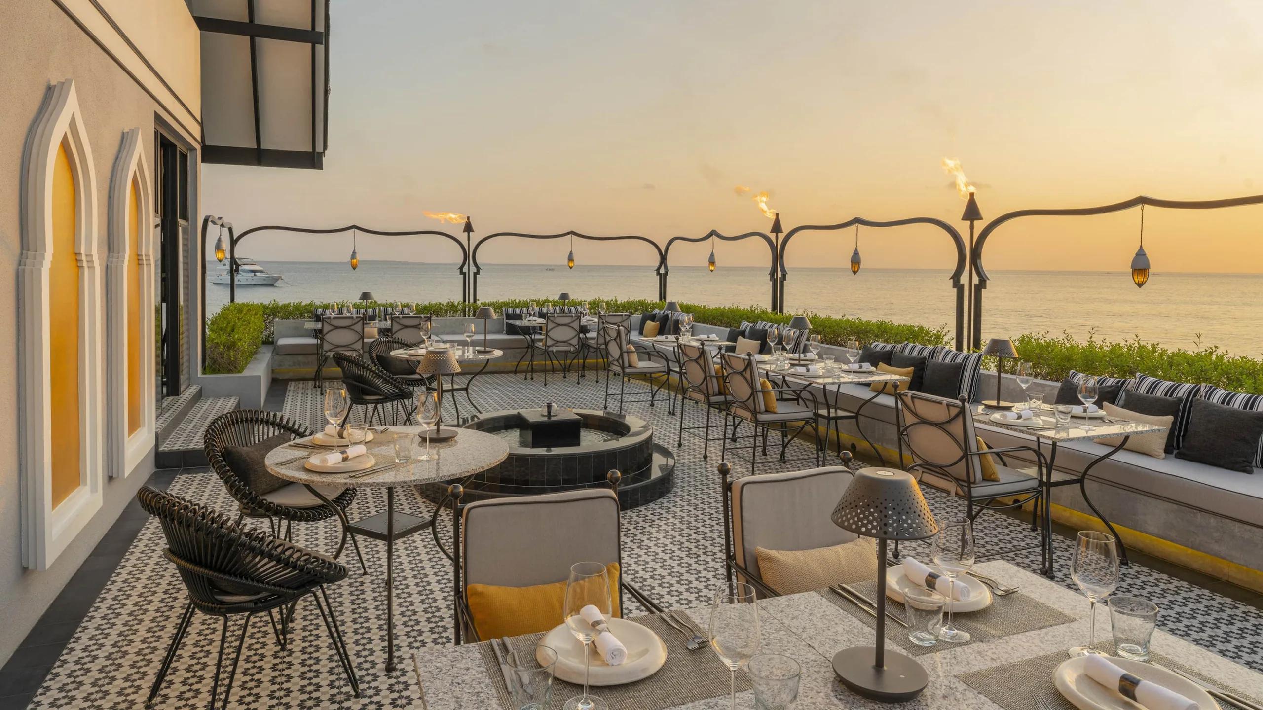 Al Barakat's terrace set for dinner at sunset, with lit torches along the railing and the ocean beyond