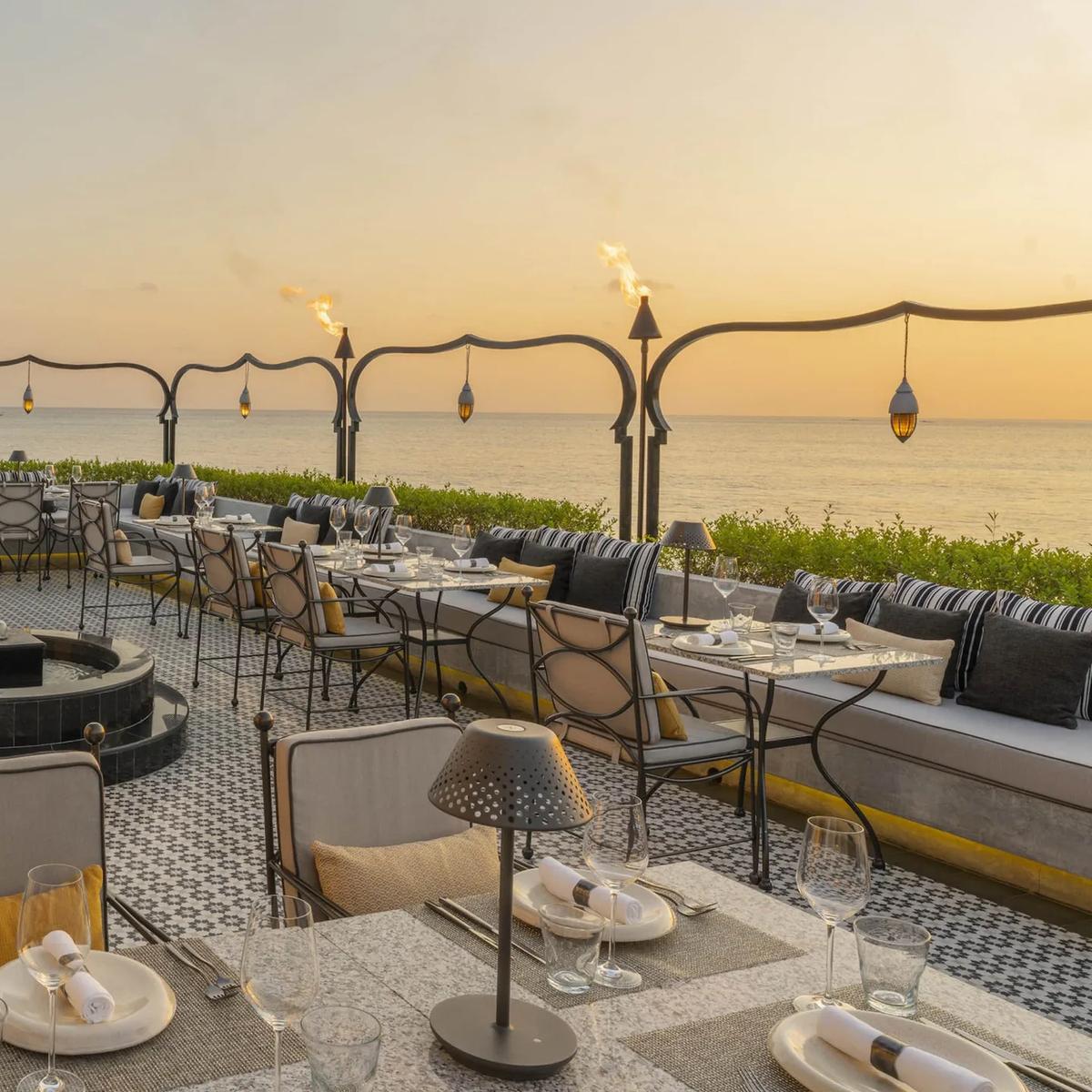 Al Barakat's terrace set for dinner at sunset, with lit torches along the railing and the ocean beyond