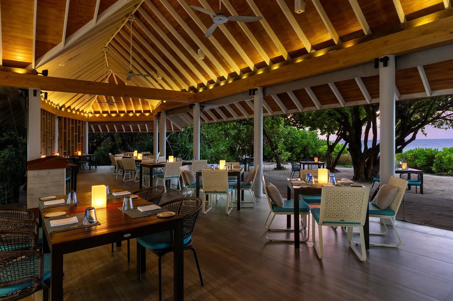Faru restaurant's open-air terrace at dusk, tables set a few steps from the shore