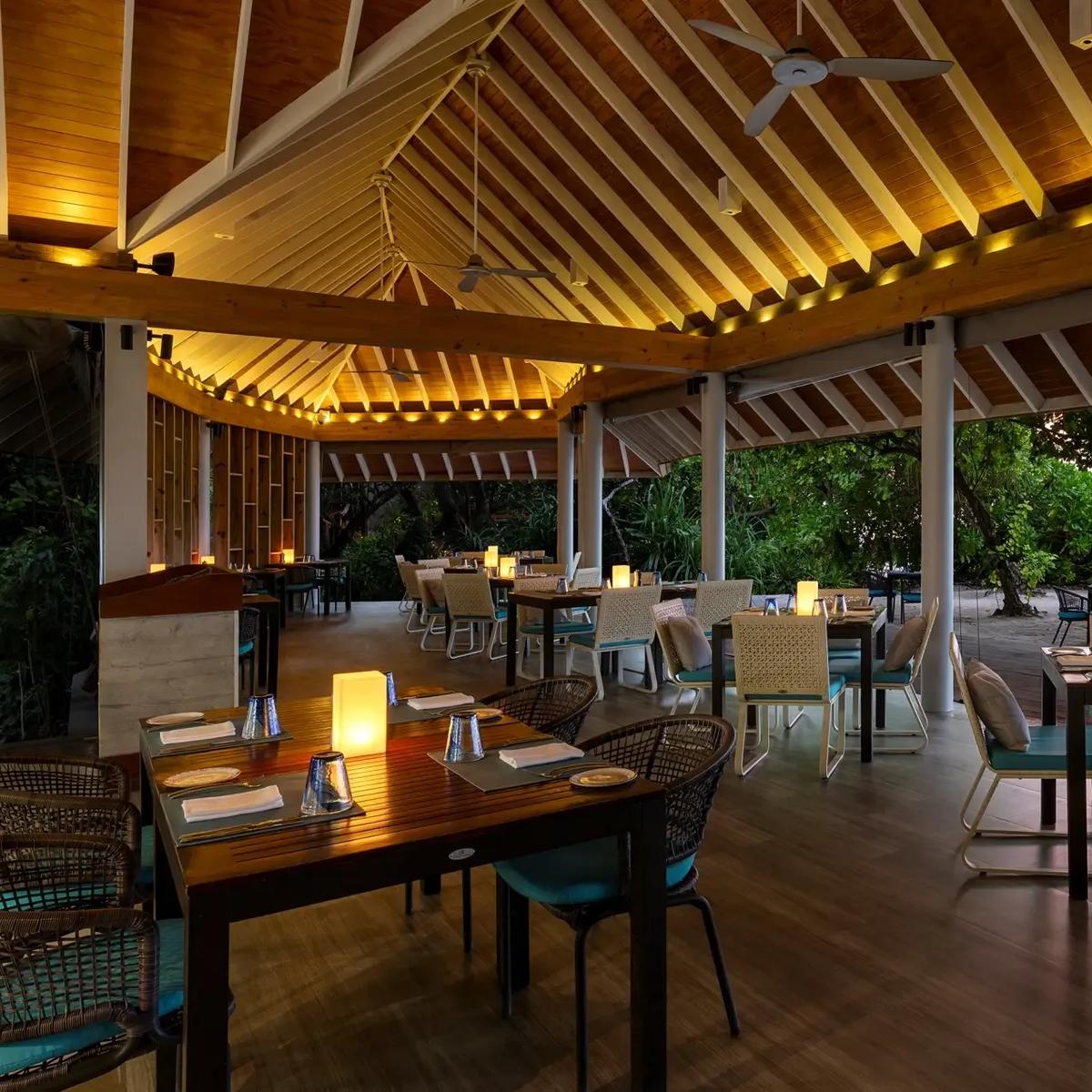 Faru restaurant's open-air terrace at dusk, tables set a few steps from the shore