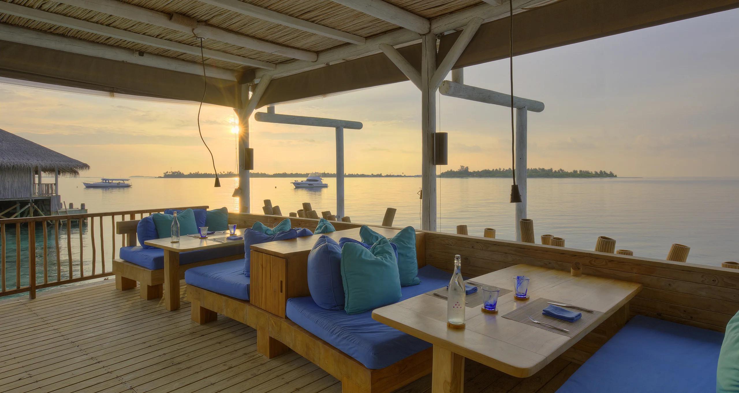 Chill Bar's thatched roof and timber beams silhouetted against a sunset sky over the reef