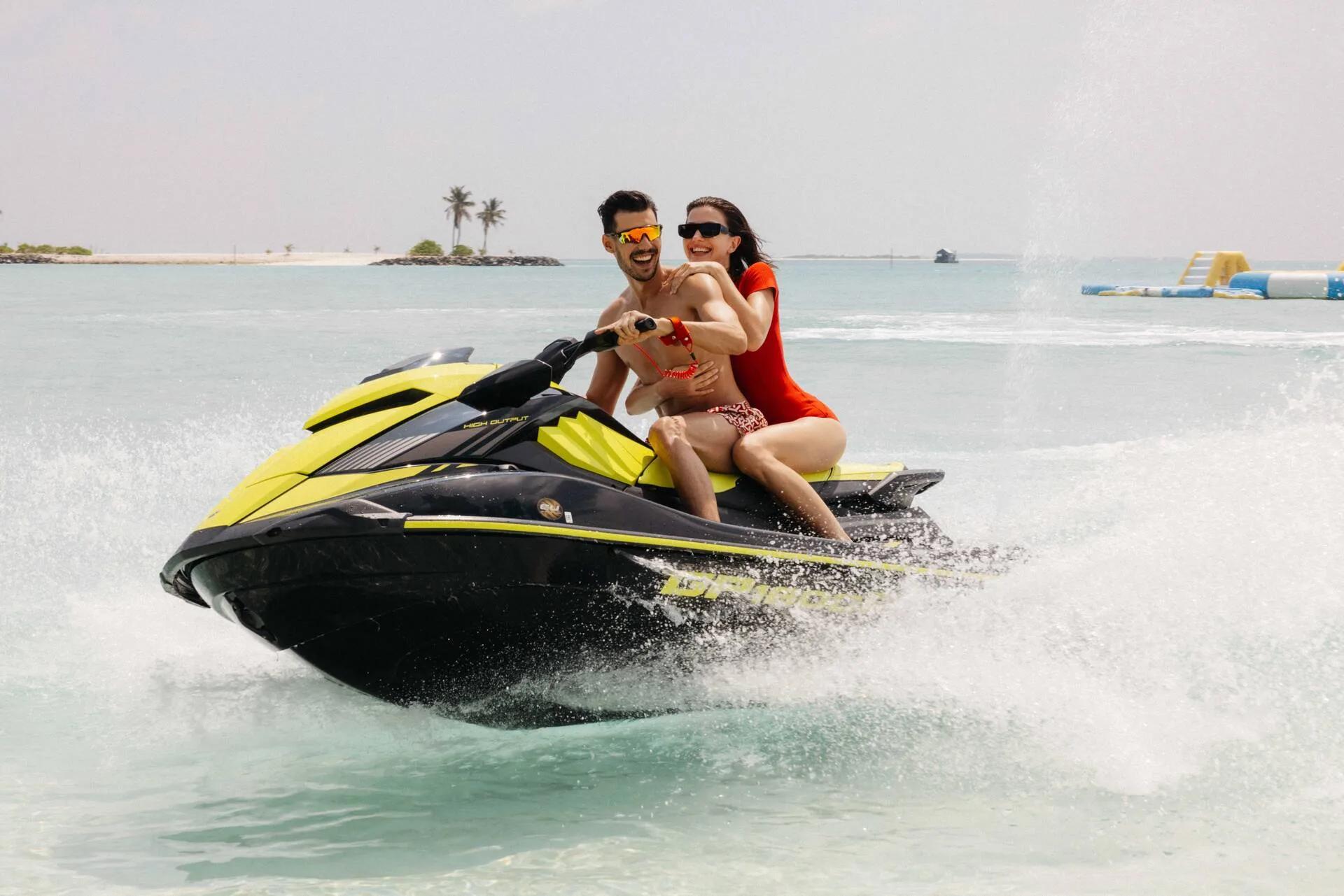 A couple riding a jet ski at speed, spray flying up behind them near a small island