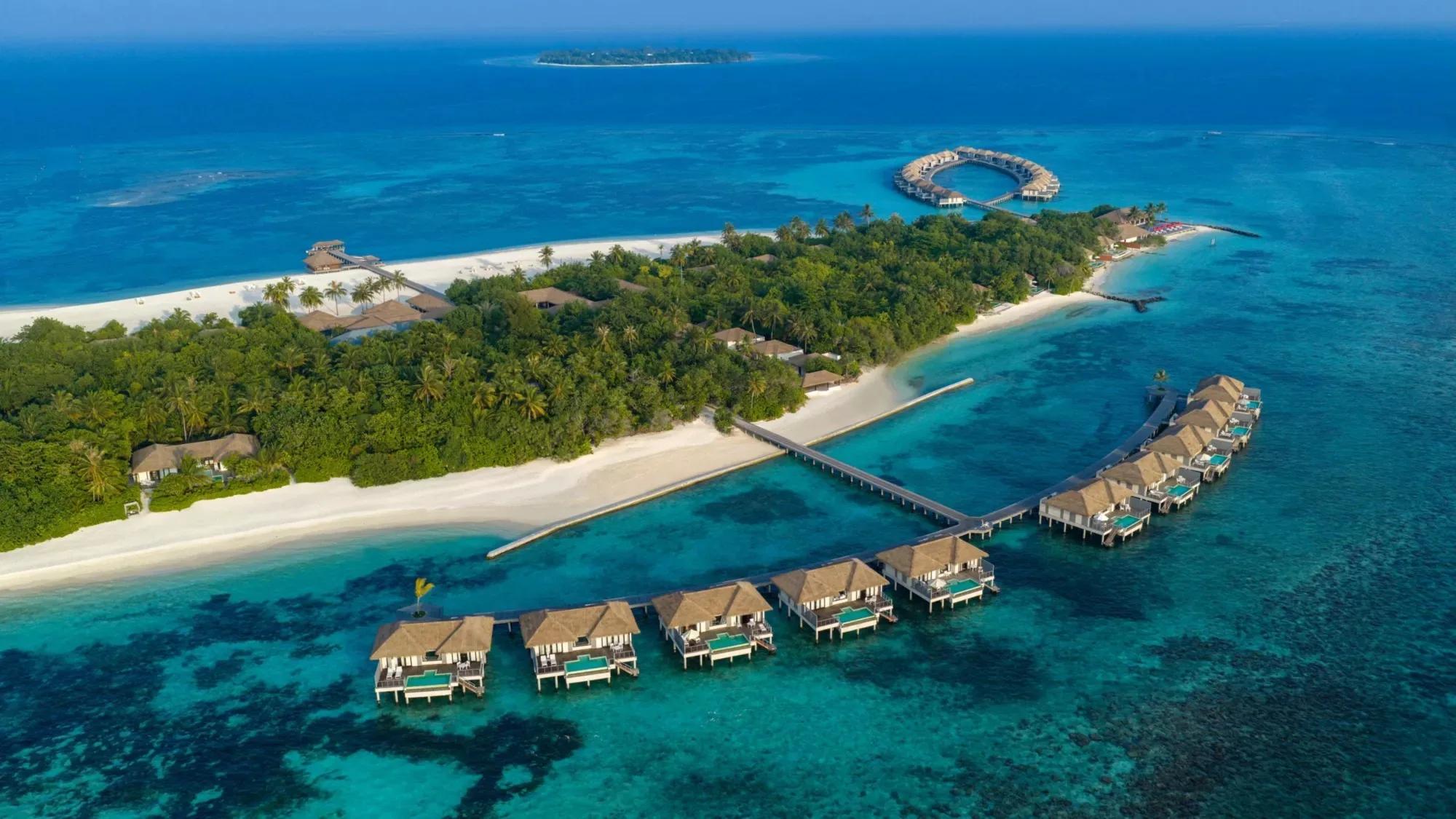Aerial view of Noku Maldives on Kuda Funafaru Island, Noonu Atoll, a circular overwater pavilion and villa jetties reaching into the reef