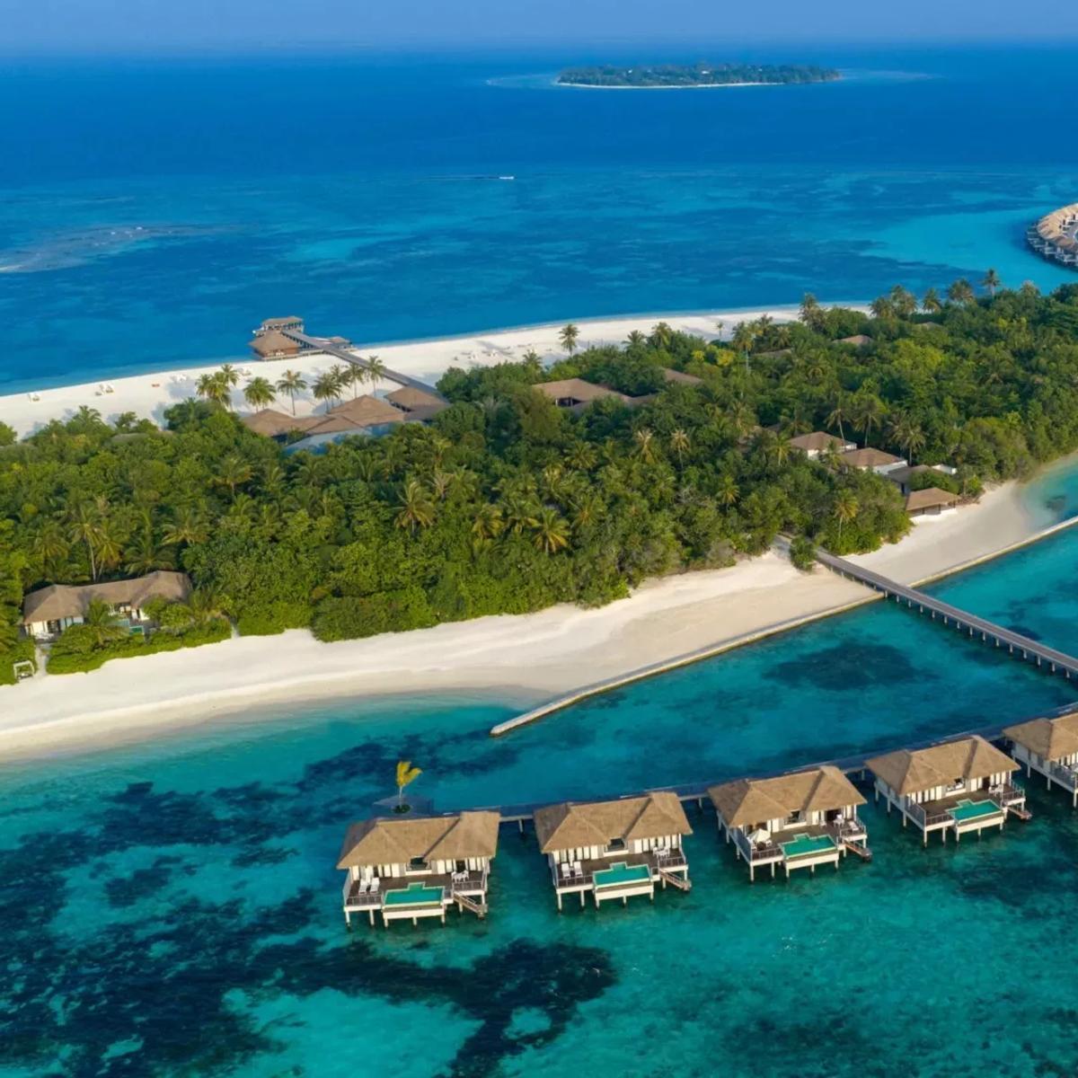 Aerial view of Noku Maldives on Kuda Funafaru Island, Noonu Atoll, a circular overwater pavilion and villa jetties reaching into the reef