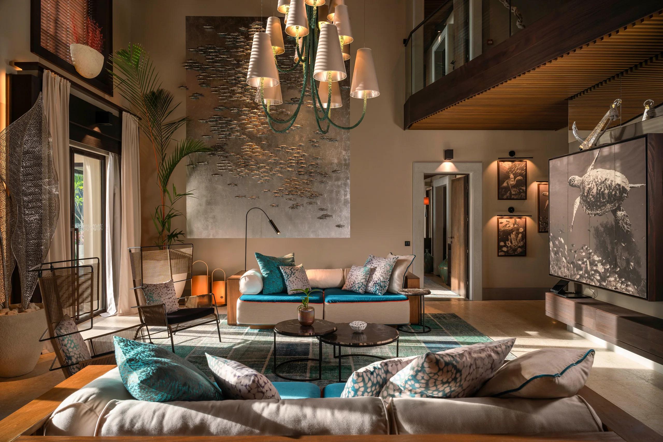 A double-height lounge inside Nirolhu Private Residence, with large-scale artwork of a sea turtle and a school of fish on the far wall