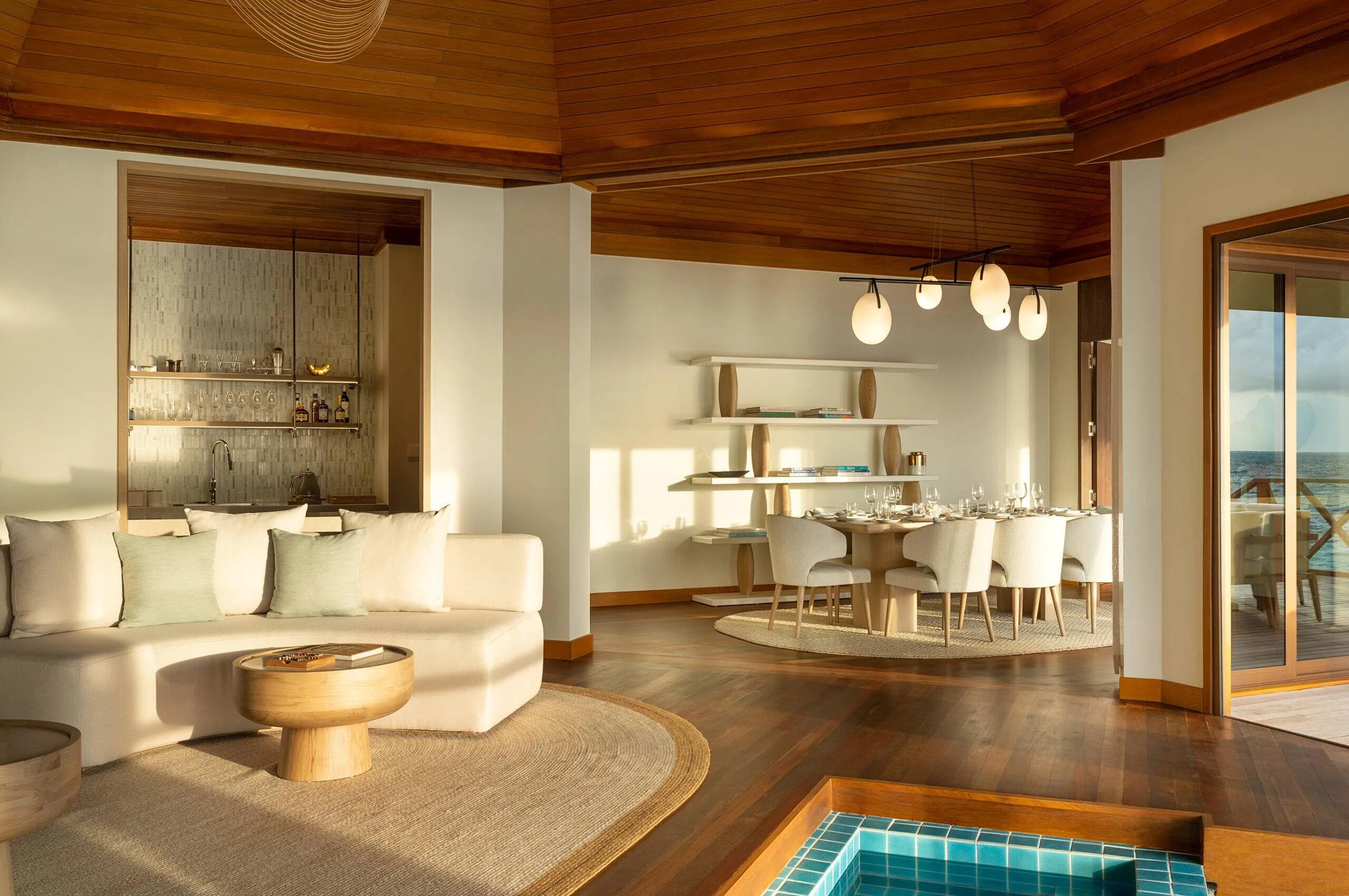 The open-plan living and dining room of a Two-Bedroom Ocean Pavilion, a stocked bar to one side and a small pool inset in the deck beyond the doors