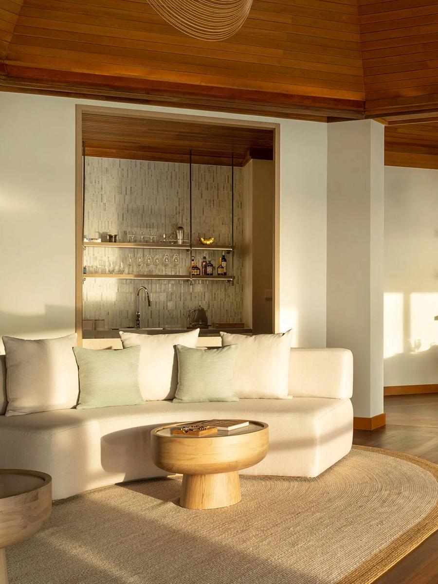 The open-plan living and dining room of a Two-Bedroom Ocean Pavilion, a stocked bar to one side and a small pool inset in the deck beyond the doors