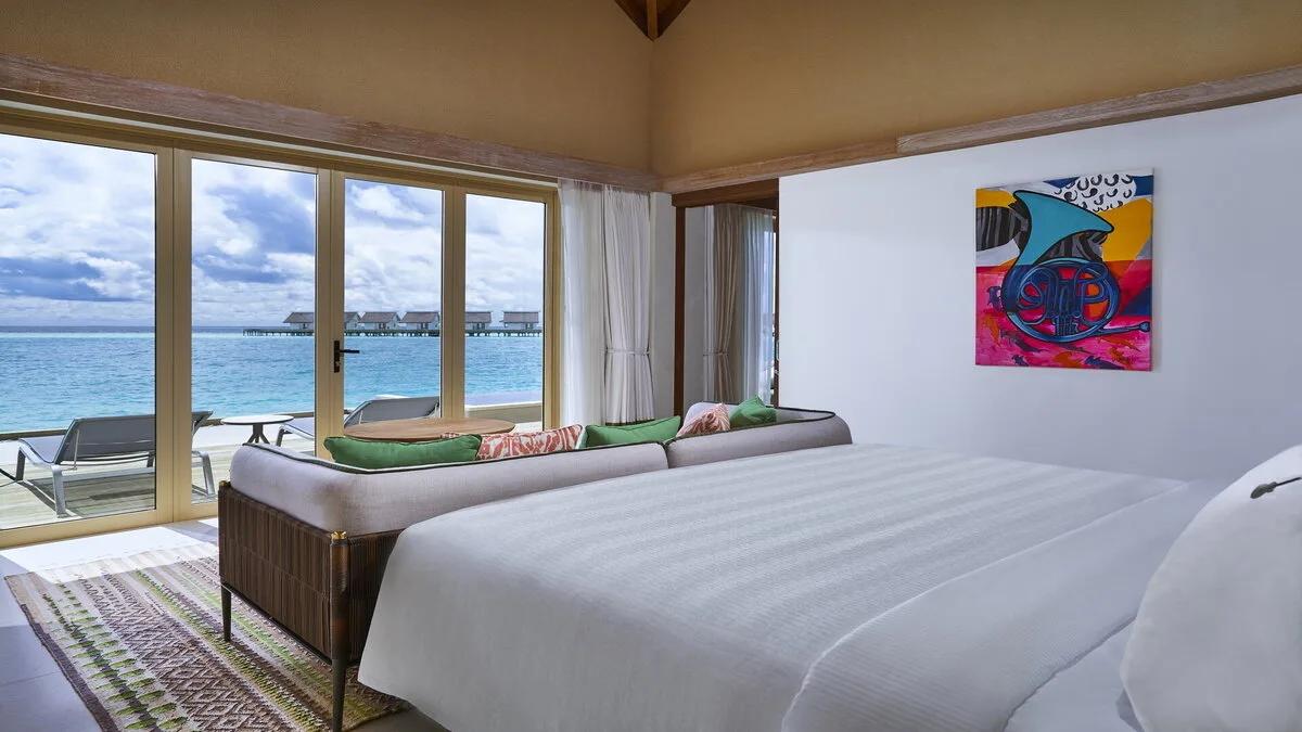 The Rock Royalty Overwater Private Pool Villa's bedroom, glass doors opening onto its private deck above the lagoon