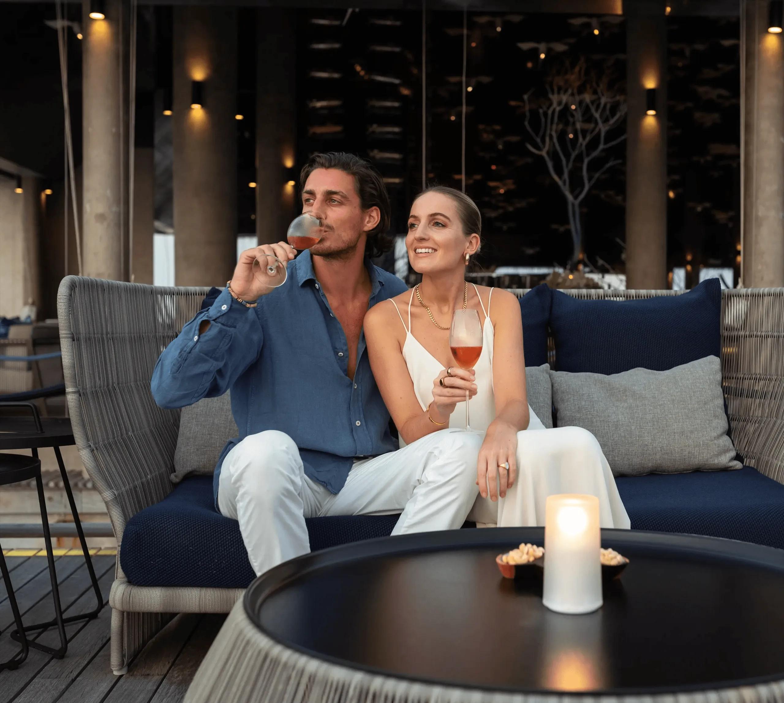 Guests relax with evening drinks in Athiri's lounge seating, candlelight and string lights overhead