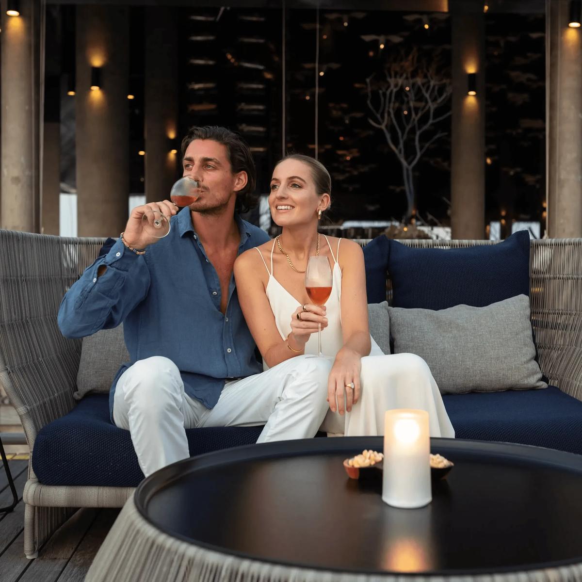 Guests relax with evening drinks in Athiri's lounge seating, candlelight and string lights overhead