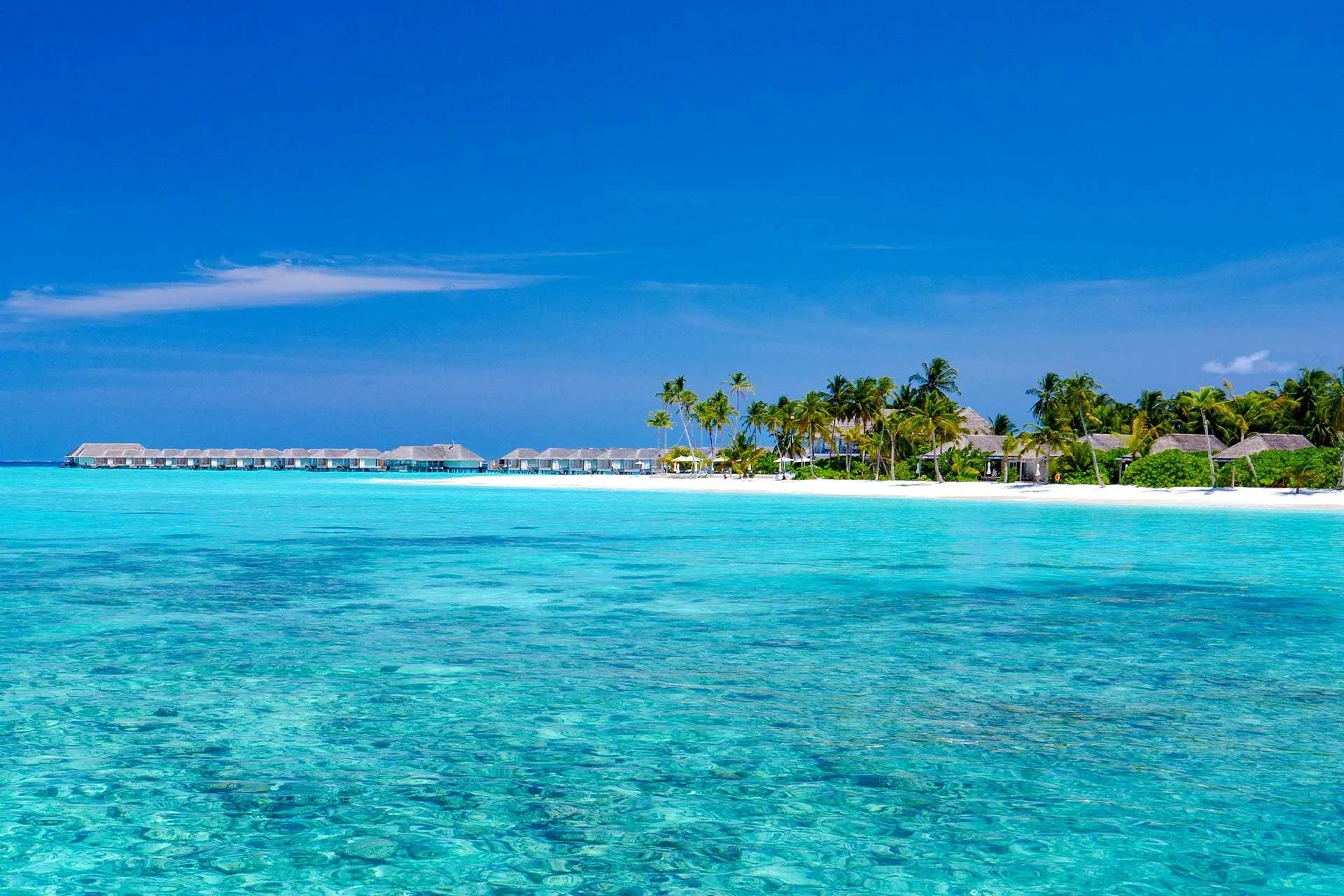 Baglioni Maldives' overwater villas and beachfront pavilions on Maagau Island, seen from the lagoon under a clear sky