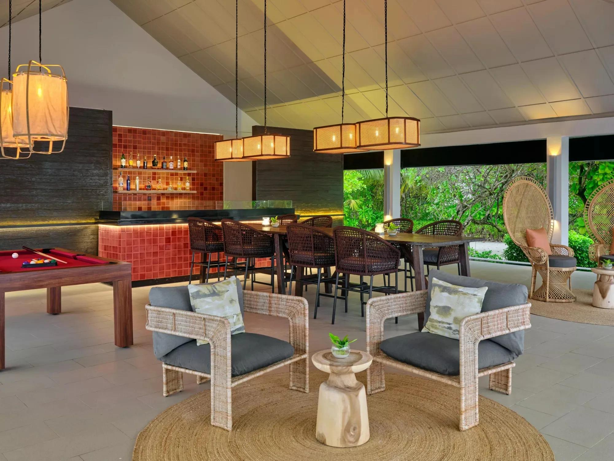 A lounge and games room at Noku Maldives, with a pool table and a tiled bar counter