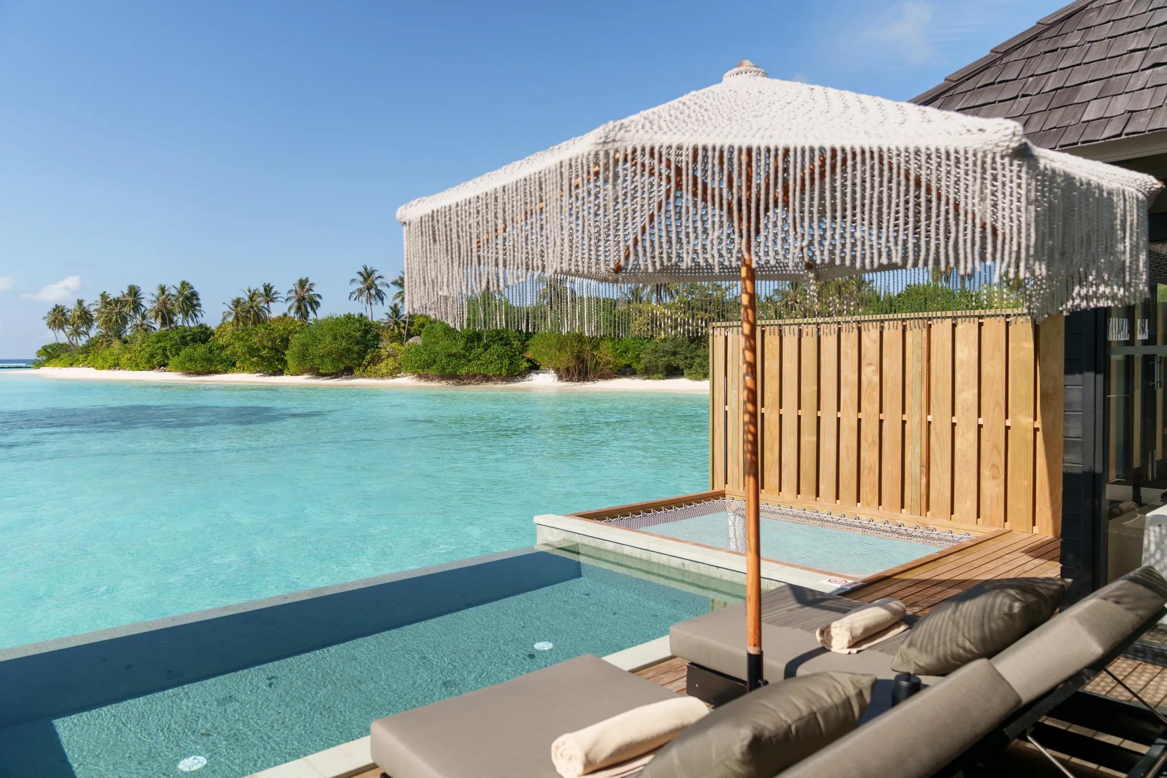 A private infinity pool blending into the lagoon at the edge of a Water Villa deck, with a netted hammock and umbrella