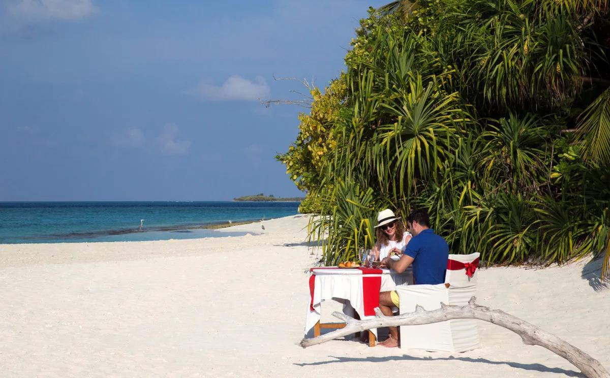 A private table set for two on the beach, screened by pandanus trees, part of the Sandbank Picnic experience