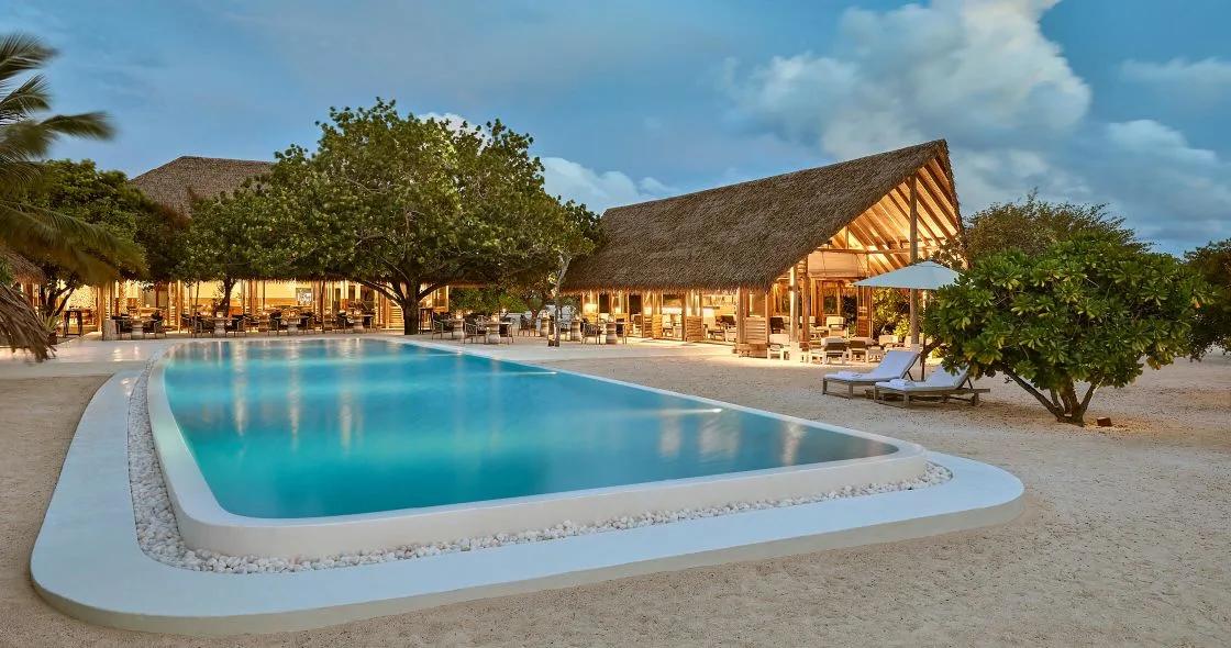 Faru Bar and the resort's 25-metre infinity-edge pool, lit at dusk beneath the trees