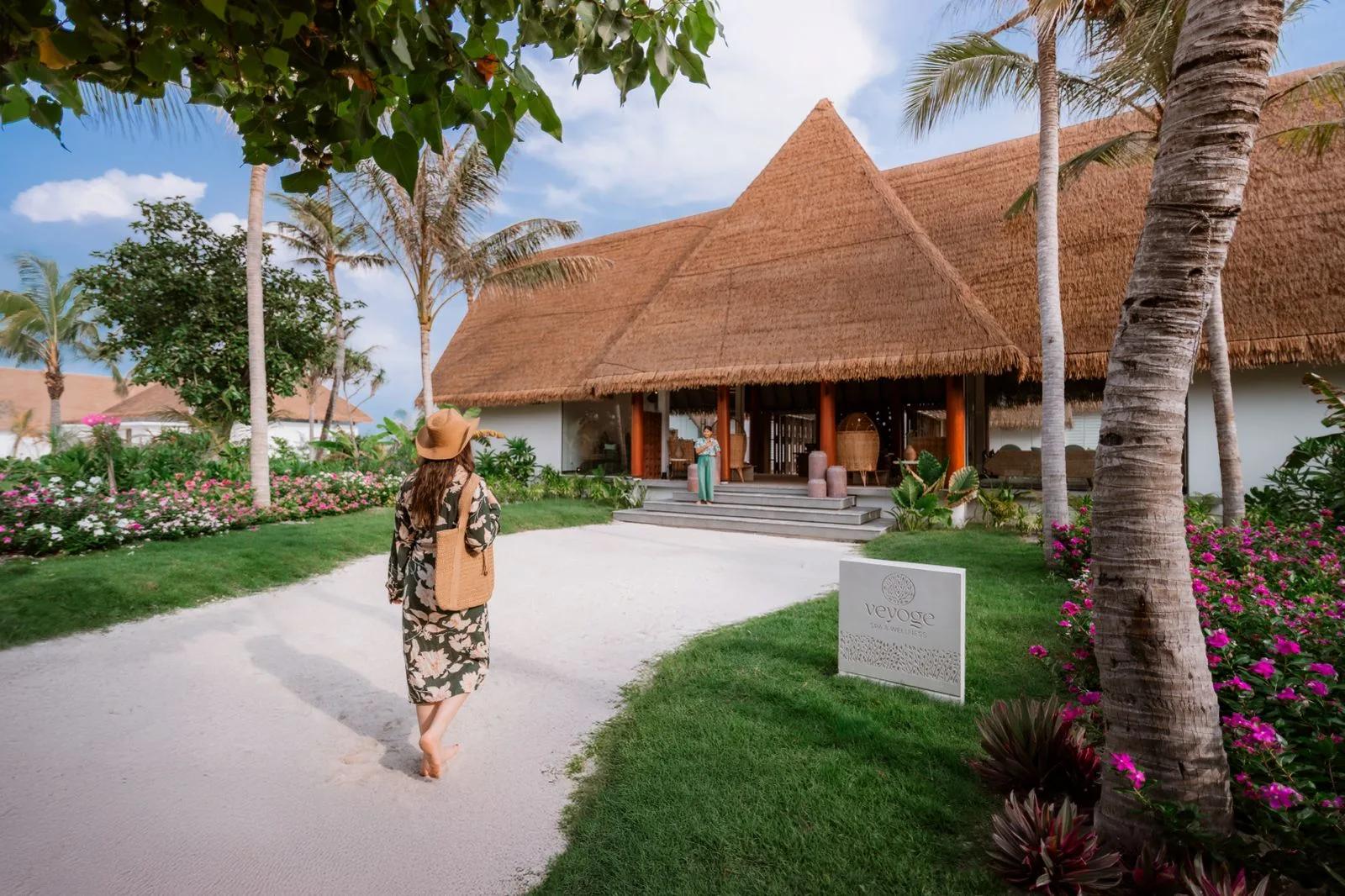 A guest walking the garden path to Veyoge Spa's thatched-roof entrance pavilion