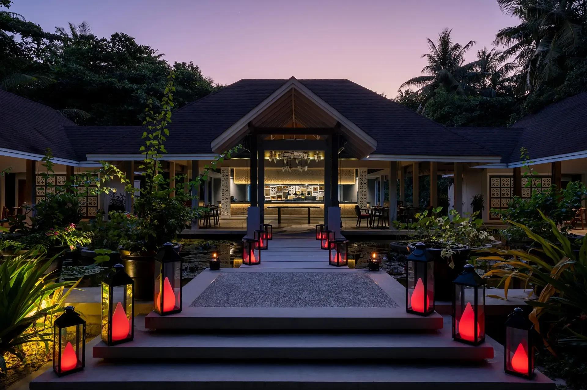 The lantern-lit walkway to Battuta at dusk, crossing a lily pond toward the open-sided dining room