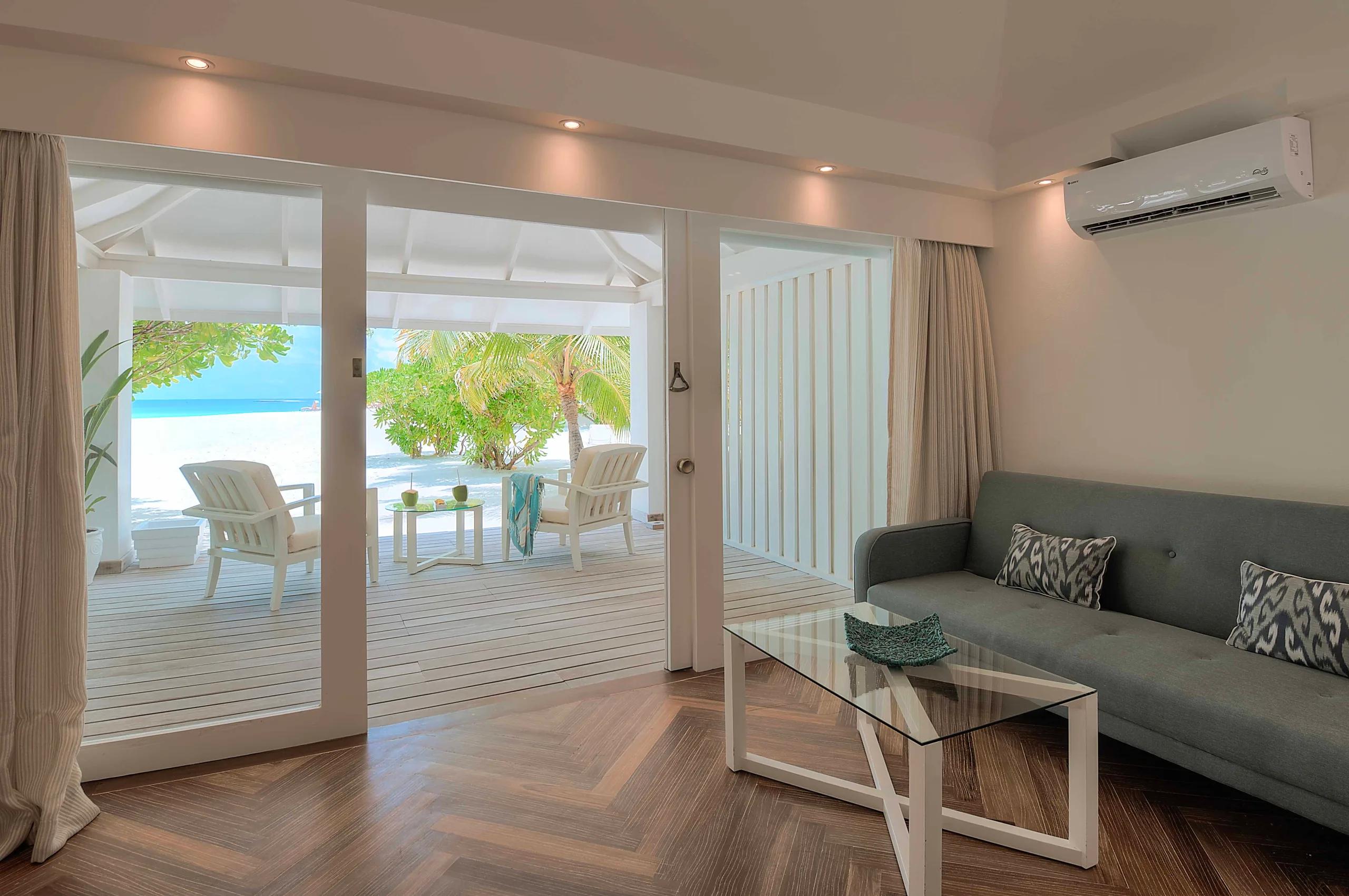 The living area of a Beach Front Junior Suite with sliding doors open to a beachfront deck and palm trees