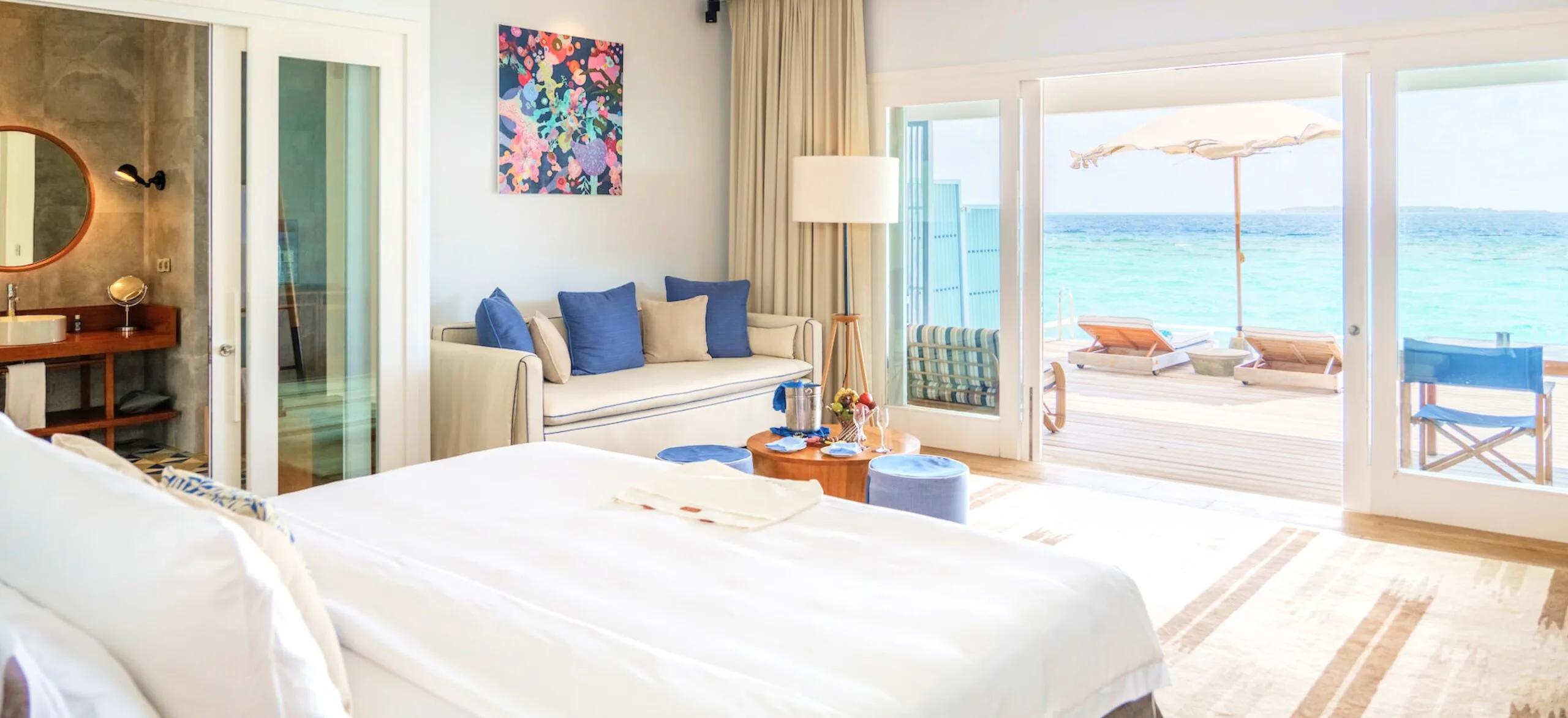 A Water Pool Villa's living area at Amilla, glass doors open to the overwater deck, pool and ocean beyond