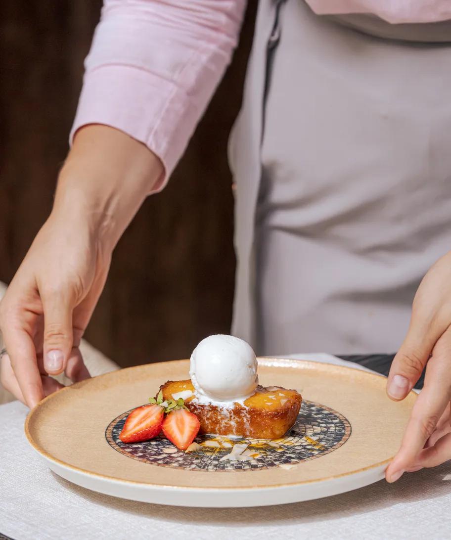A waiter presenting a caramelised dessert with ice cream and strawberries tableside — La Joie photograph to follow