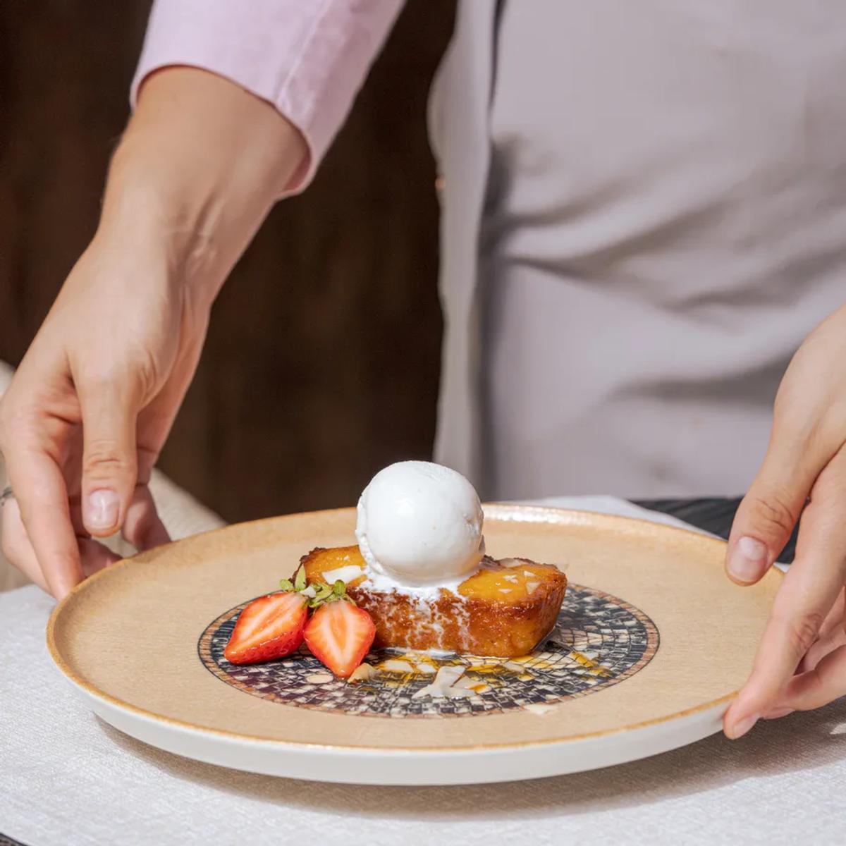 A waiter presenting a caramelised dessert with ice cream and strawberries tableside — La Joie photograph to follow