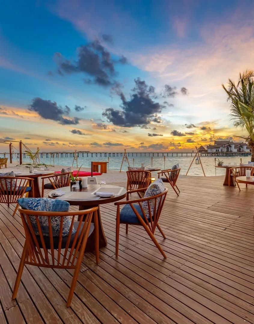 Vista del Mar's beachfront dining tables set for sunset, with the resort's overwater jetty in the distance