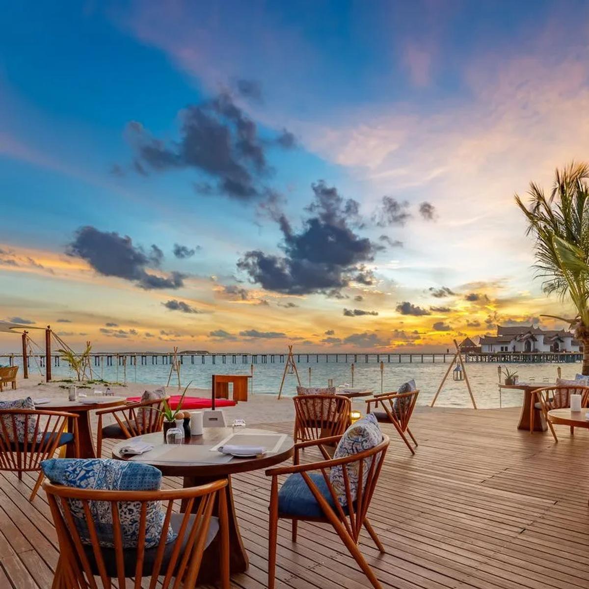 Vista del Mar's beachfront dining tables set for sunset, with the resort's overwater jetty in the distance