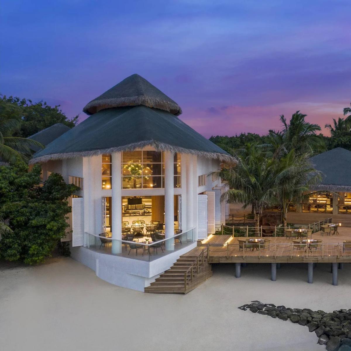 Aailaa restaurant at dusk, its thatched dining pavilion and pool deck lit up beside the beach