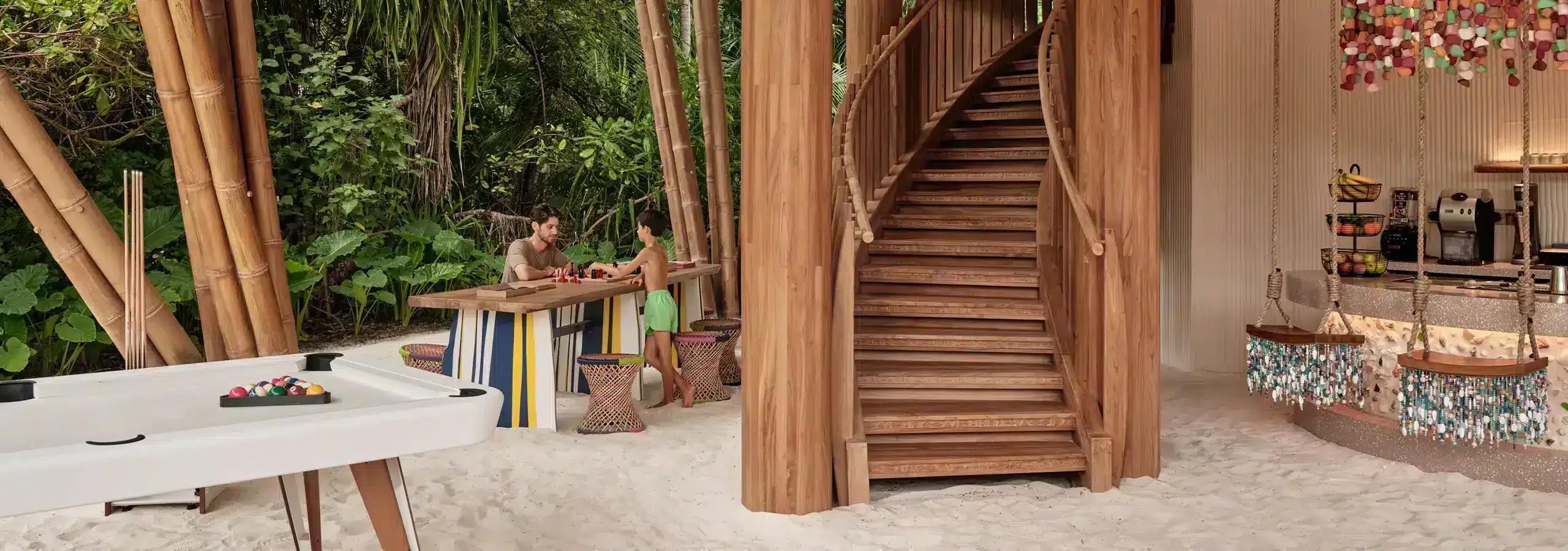 Teens Hut's games room, with a pool table and a curved timber staircase, set among bamboo trees and beaded swing seats