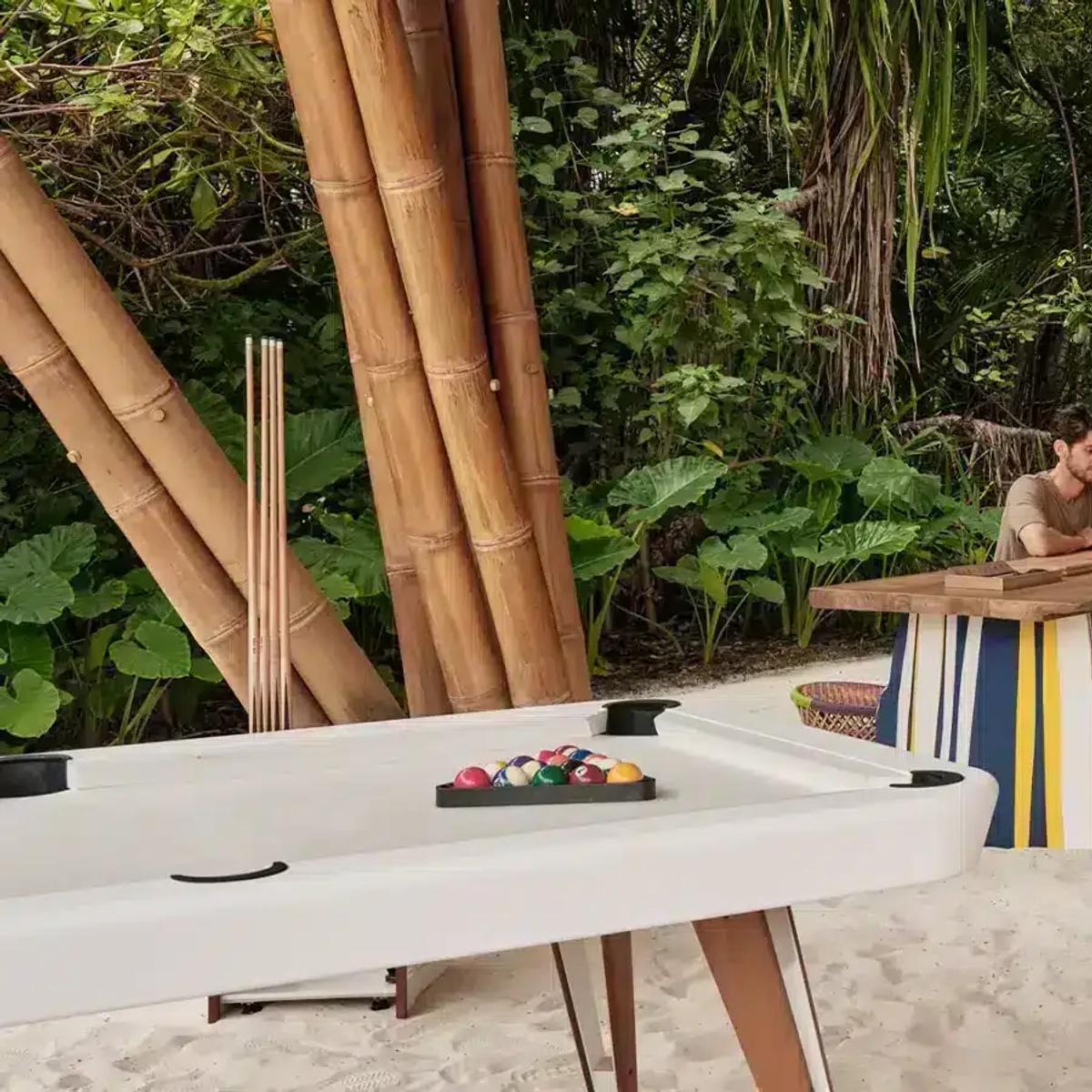 Teens Hut's games room, with a pool table and a curved timber staircase, set among bamboo trees and beaded swing seats