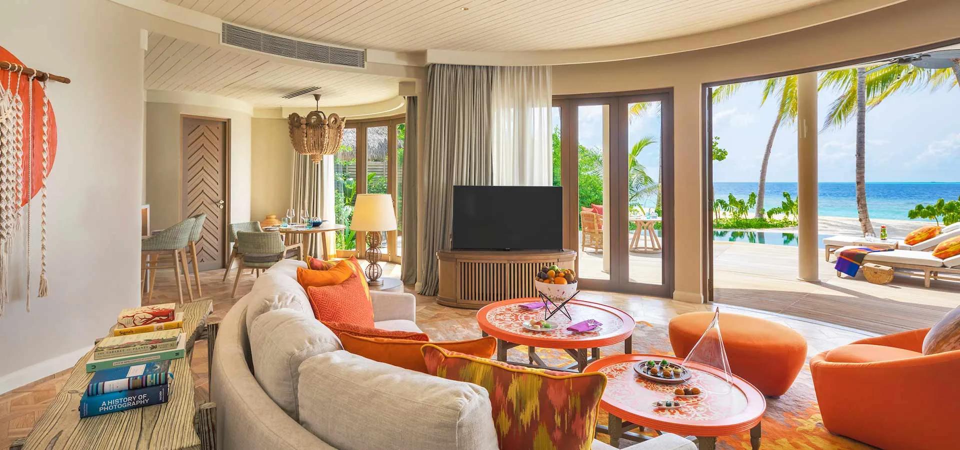A Beach Residence living room opening onto its private pool, sun loungers, palm trees and the ocean beyond.