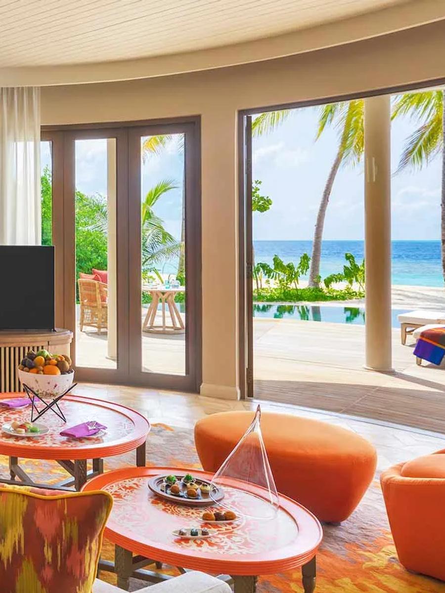 A Beach Residence living room opening onto its private pool, sun loungers, palm trees and the ocean beyond.
