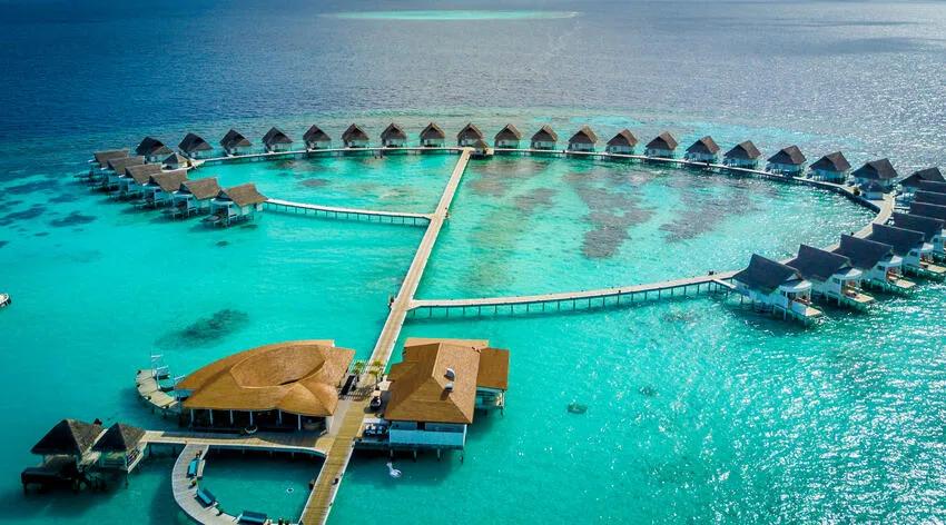 An elevated view of the overwater villa row with the island and its jetty behind