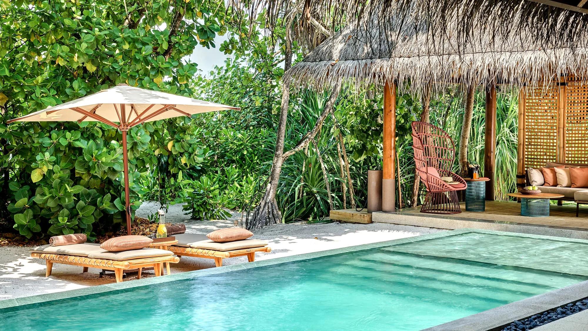 The pool deck of a Luxury Beach Villa with Pool, screened by tropical greenery, with a woven rattan chair beside the water