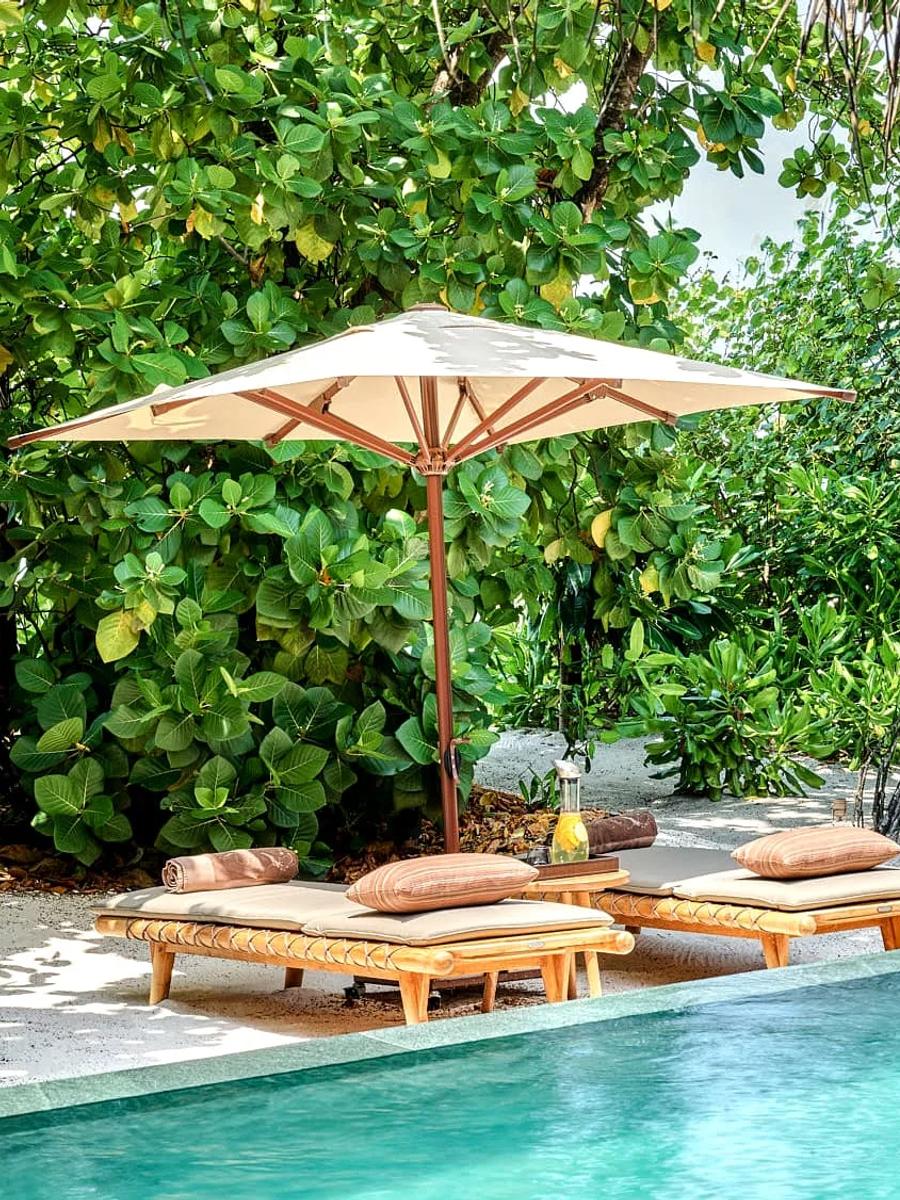 The pool deck of a Luxury Beach Villa with Pool, screened by tropical greenery, with a woven rattan chair beside the water