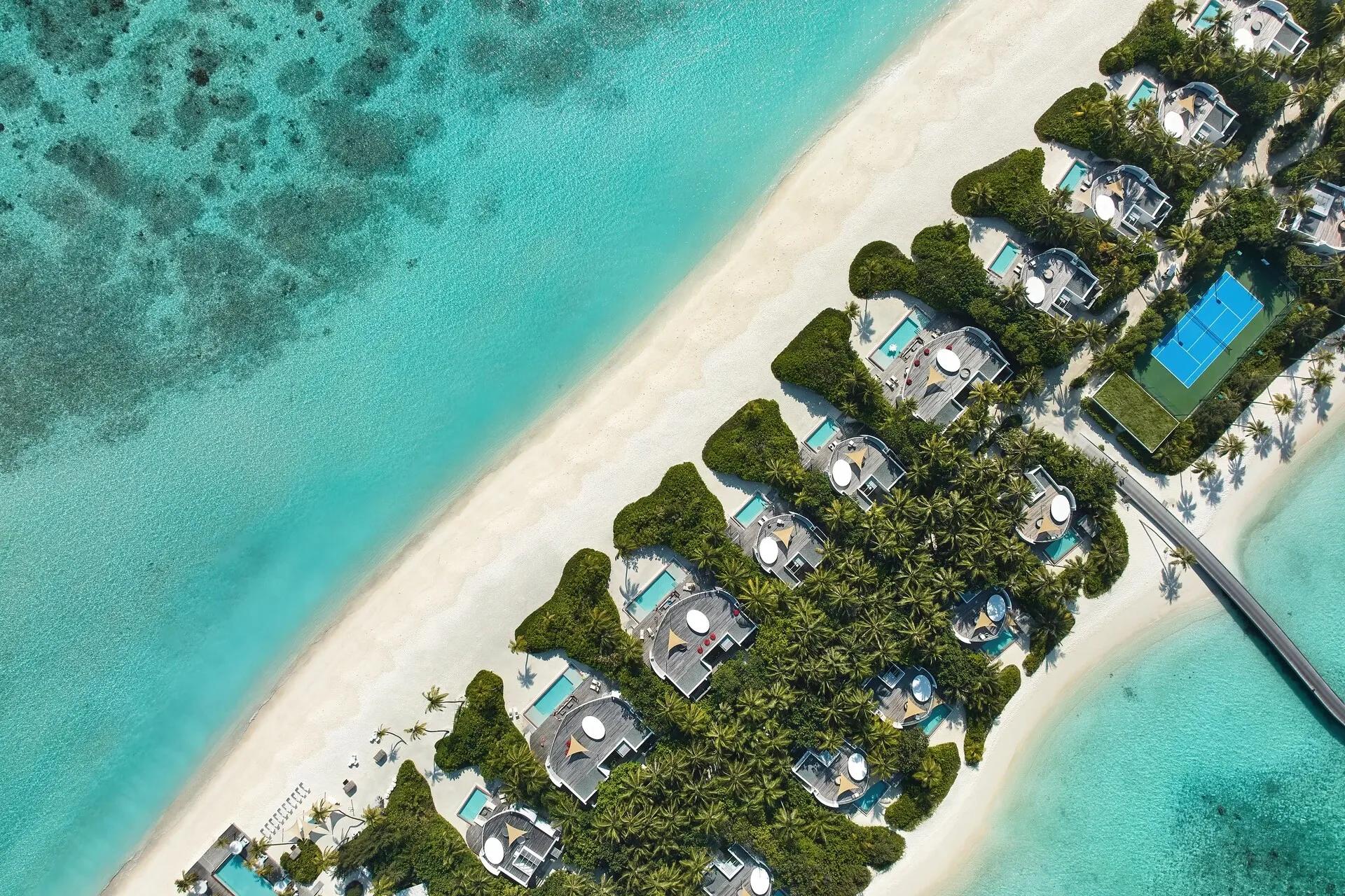 Aerial view of Jumeirah Olhahali Island's beachfront villa row, reef-fringed lagoon, and boardwalk leading out to the overwater villa cluster