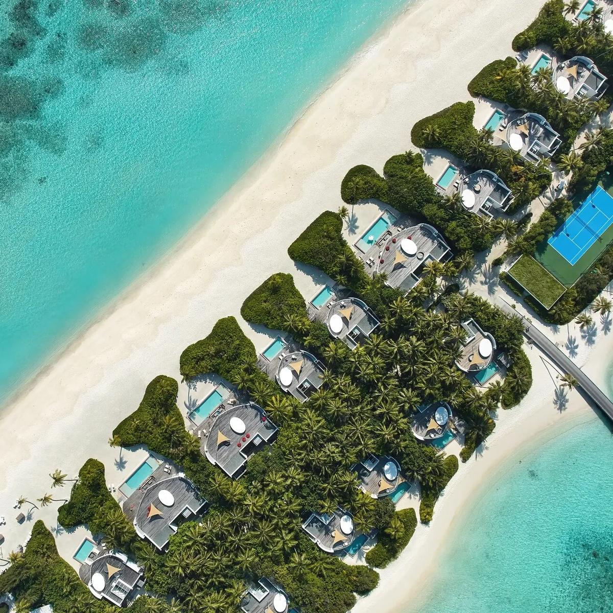 Aerial view of Jumeirah Olhahali Island's beachfront villa row, reef-fringed lagoon, and boardwalk leading out to the overwater villa cluster