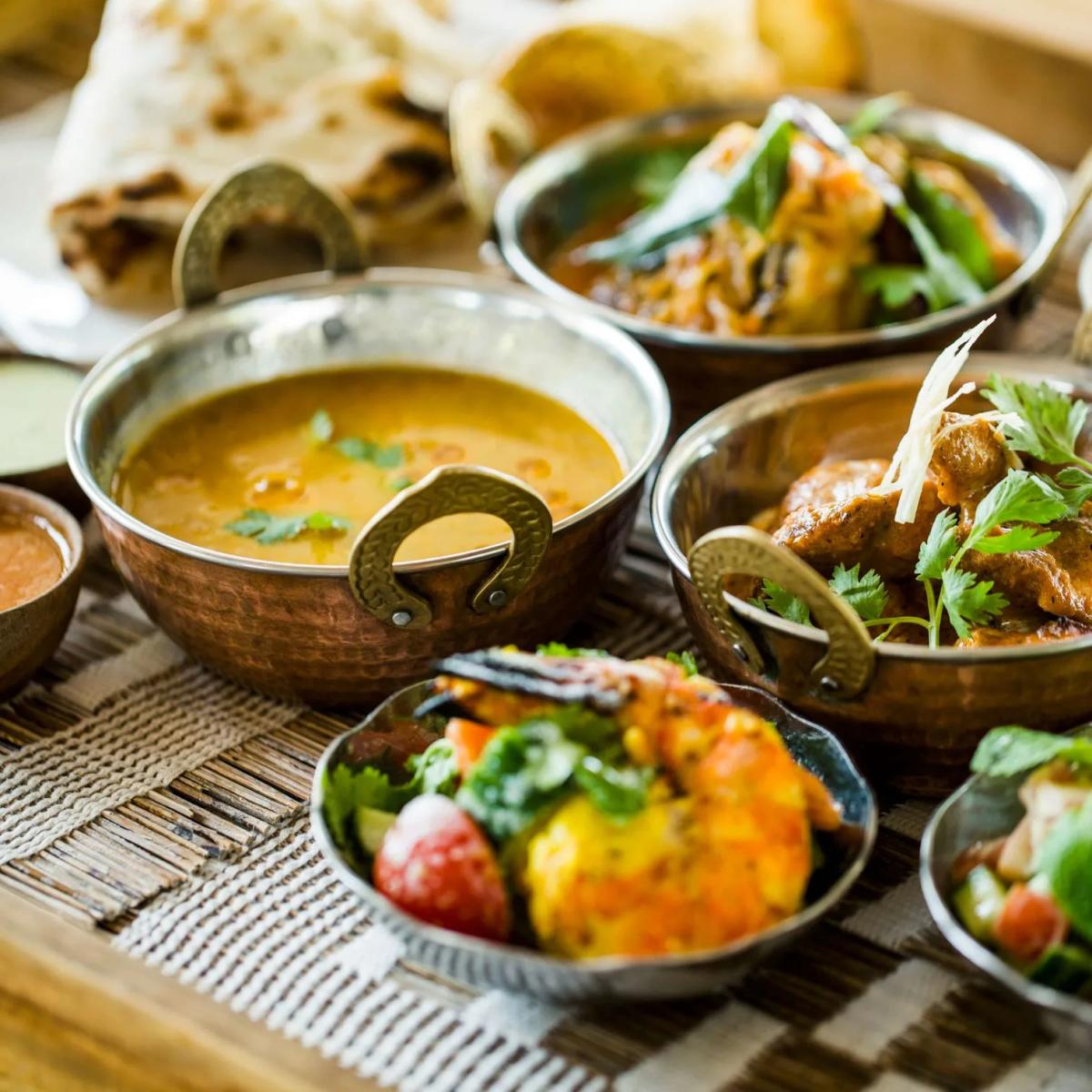 Copper bowls of curry, rice, prawns and flatbread laid out on a woven table mat