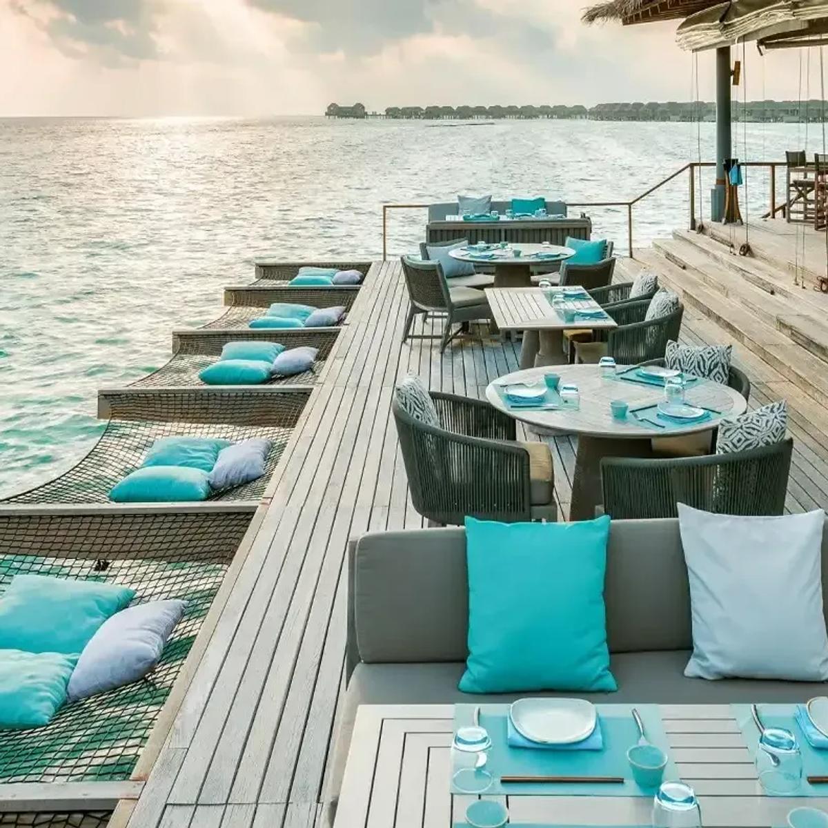 Lagoon Bar's overwater dining deck, hammock-style day beds and cushioned seating strung along the jetty above turquoise water