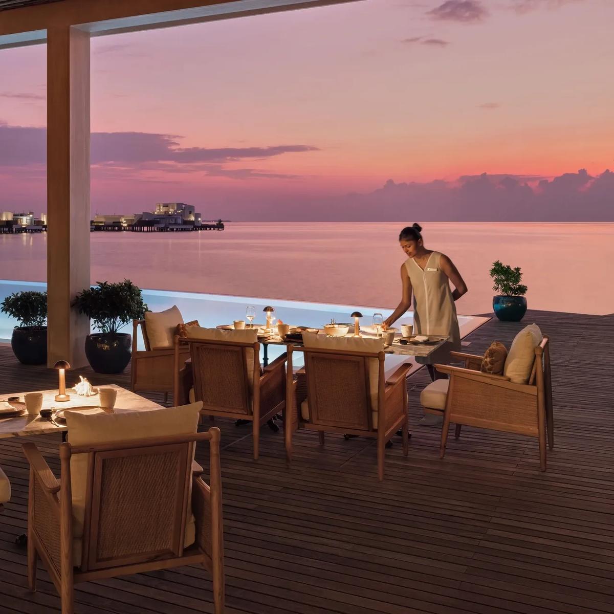 A dining terrace at dusk beside an infinity pool, overwater villas visible across the water — Alaaya Bay has no dedicated photograph in the source material; this stands in as the closest available shoreline dining scene