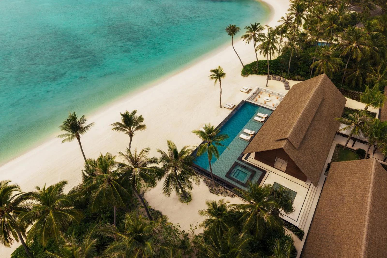 Aerial view of a Grand Residence at One&Only Reethi Rah, its private pool and thatched roof set beside a curve of beach