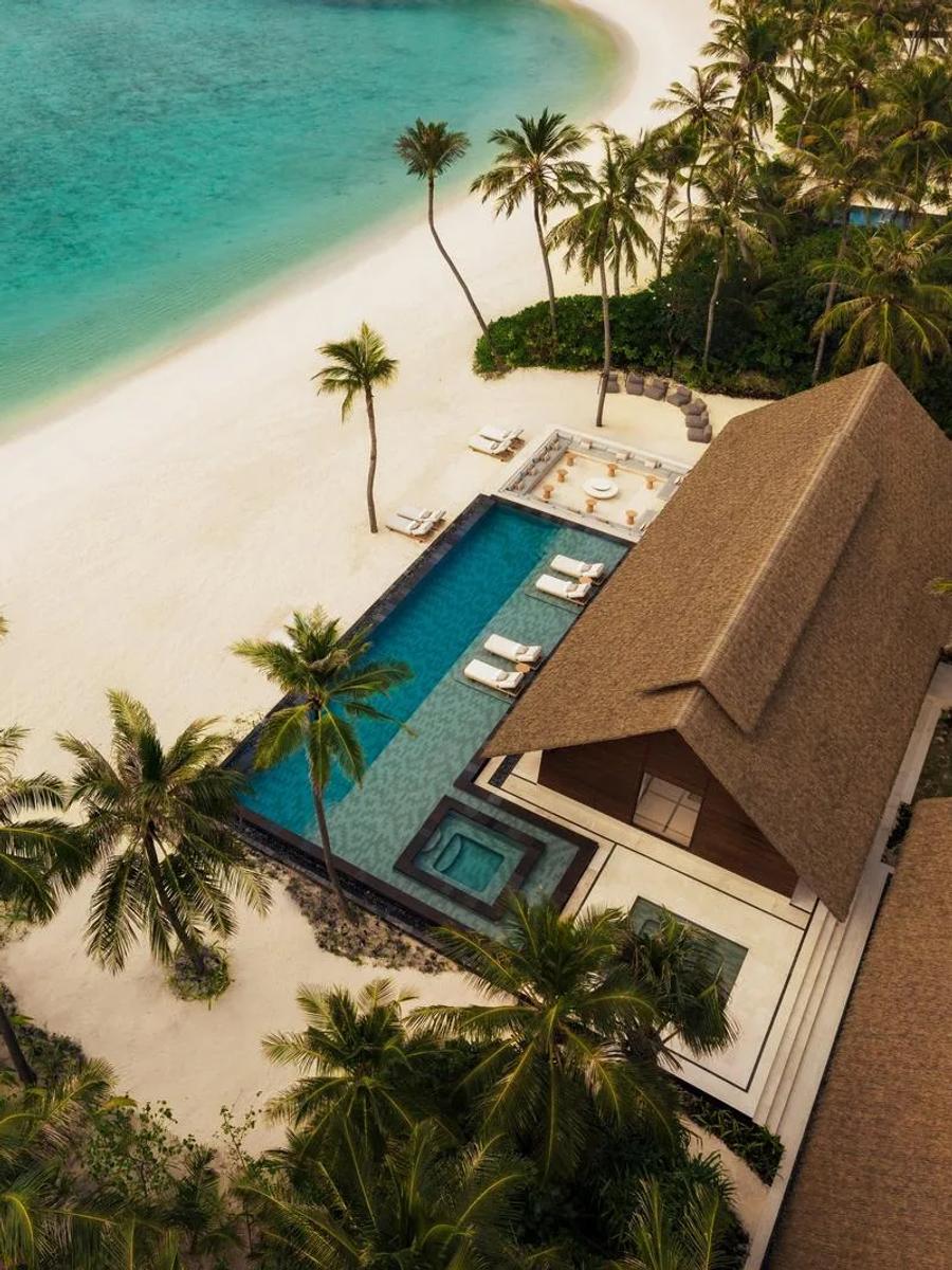 Aerial view of a Grand Residence at One&Only Reethi Rah, its private pool and thatched roof set beside a curve of beach