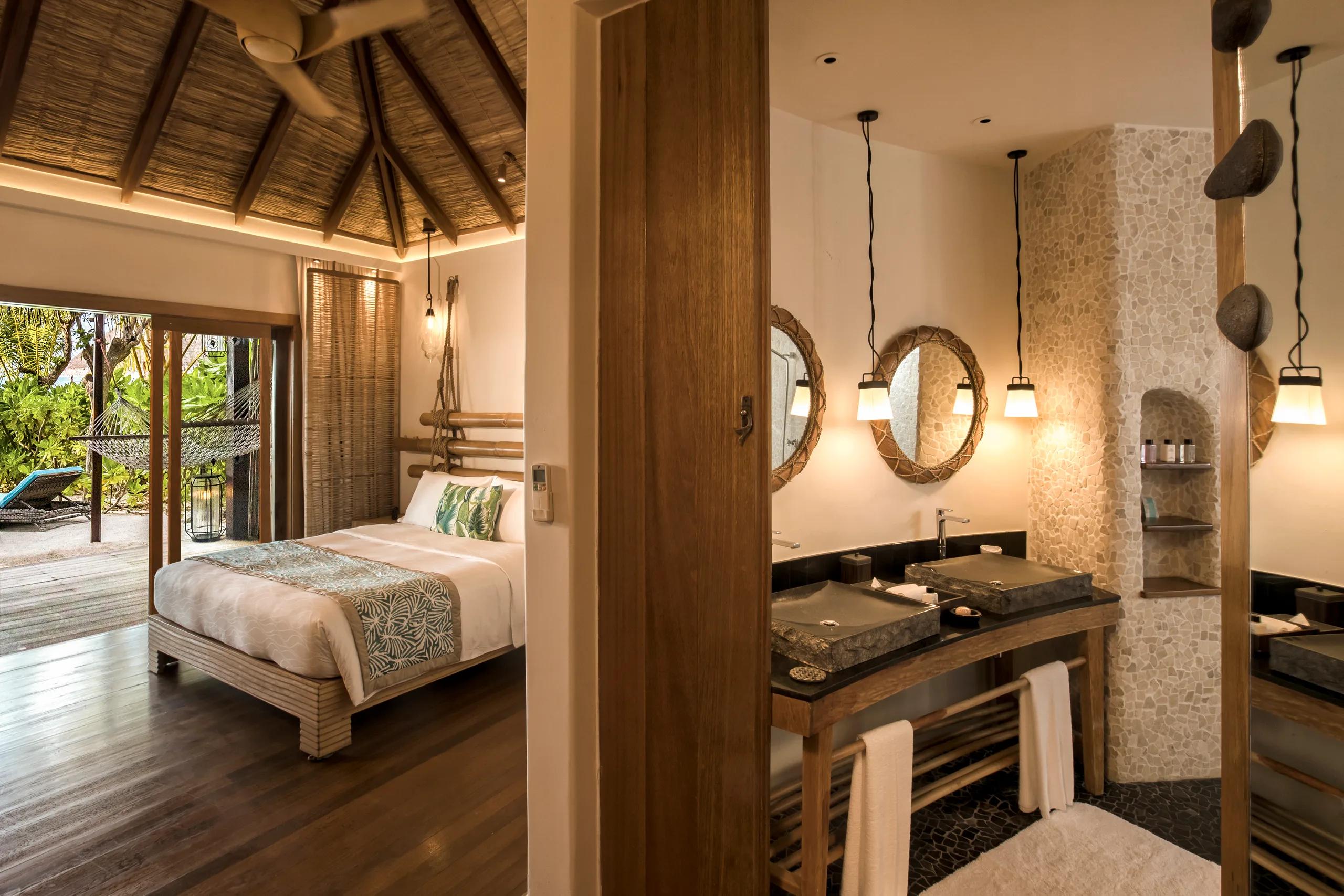 Beach Villa bedroom with a bamboo headboard opening onto a garden terrace, ensuite bathroom with twin stone basins beyond