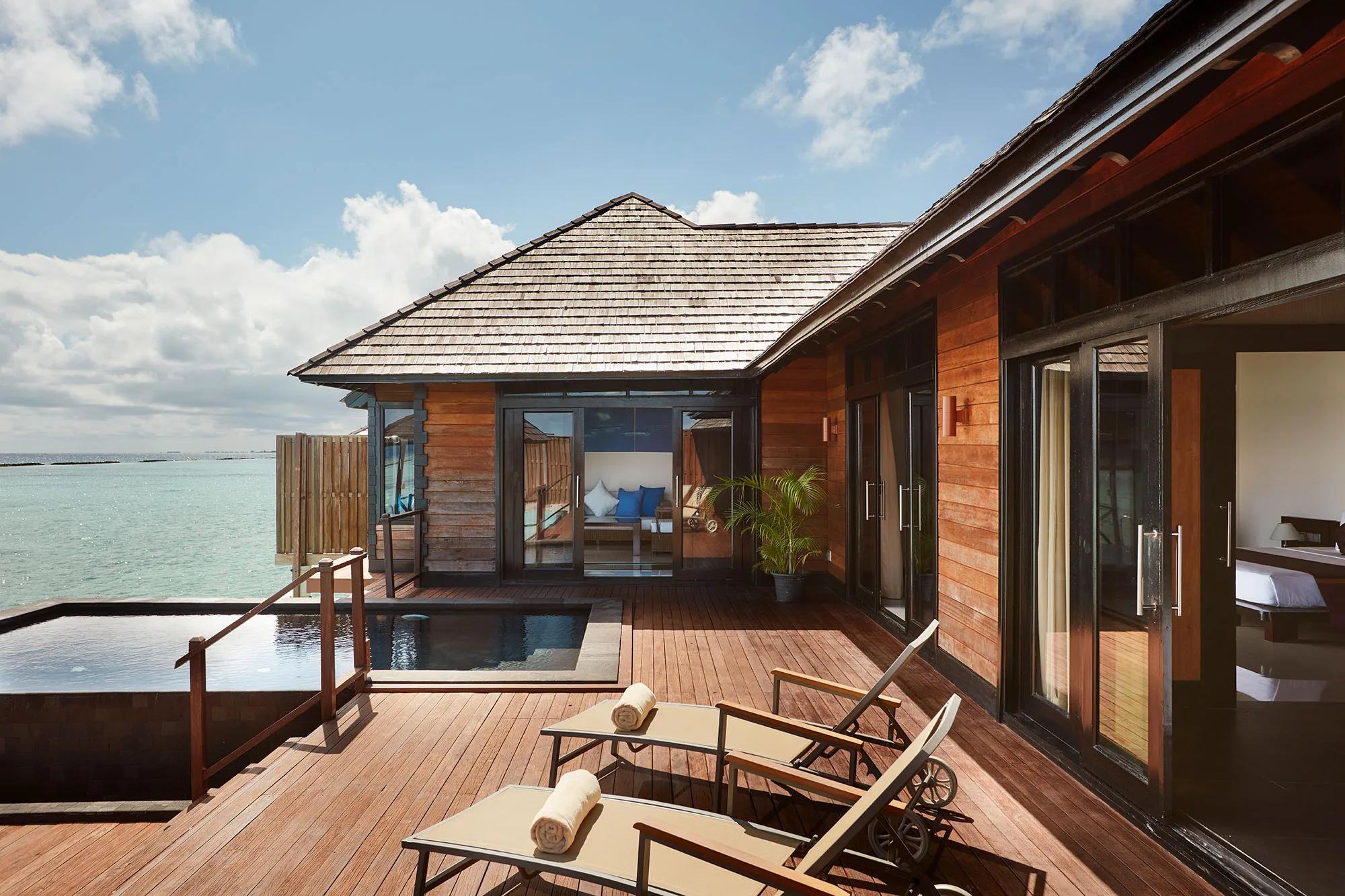 An overwater deck with a private pool and sun loungers at an Infinity Water Villa, glass doors open to the bedroom
