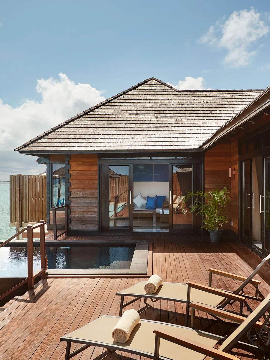 An overwater deck with a private pool and sun loungers at an Infinity Water Villa, glass doors open to the bedroom